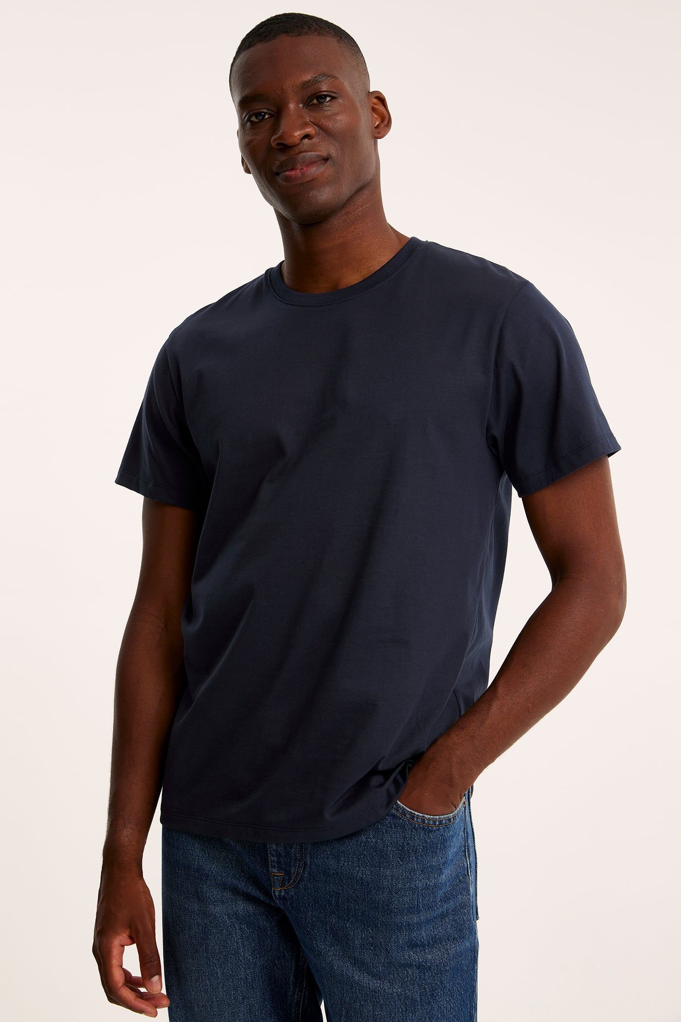 Frontvy av en man i en mörkblå rundhalsad bomulls-t-shirt och blå jeans.
