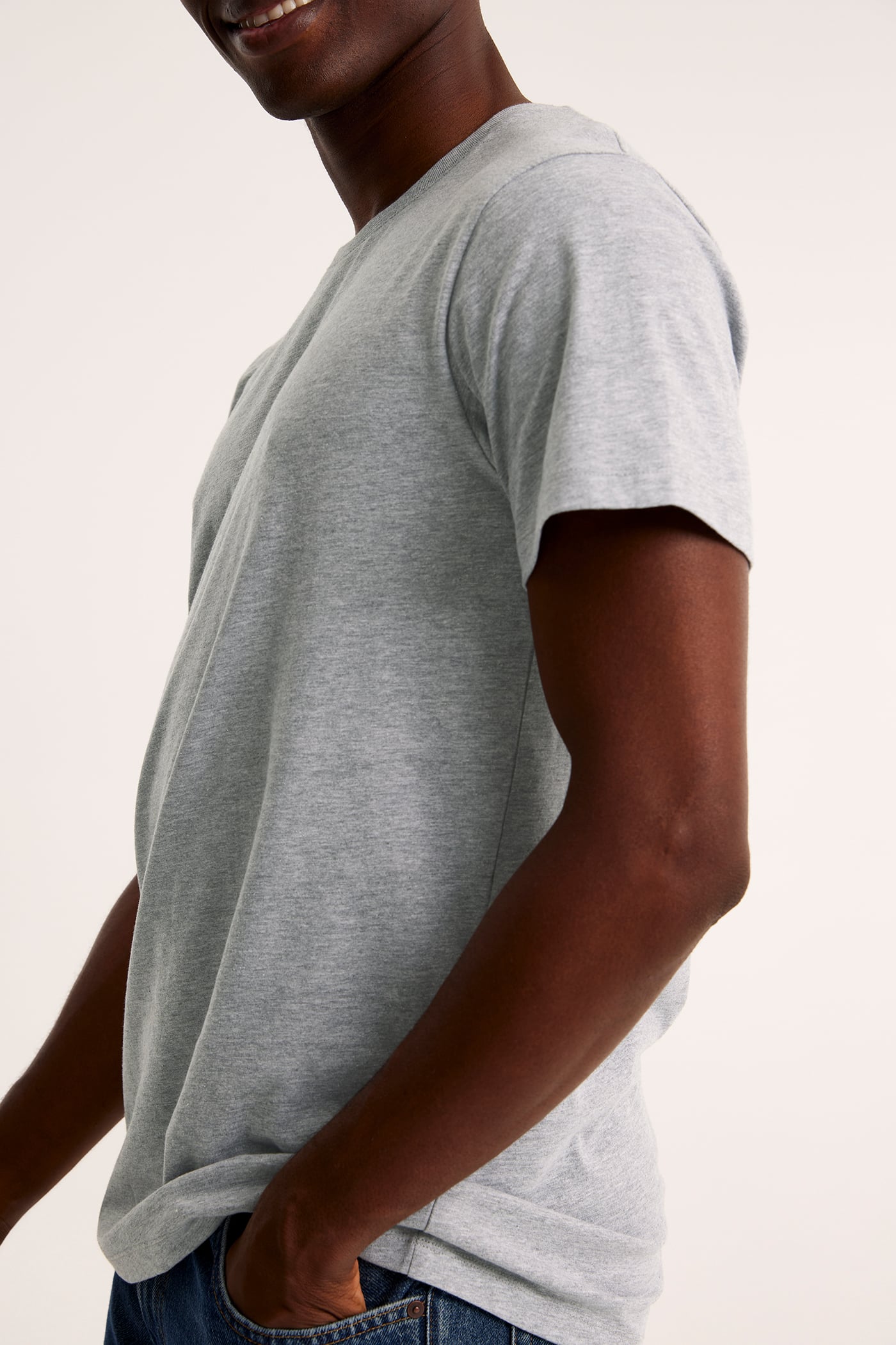Sidovy av en man i melerad ljusgrå rundhalsad t-shirt och blå jeans.