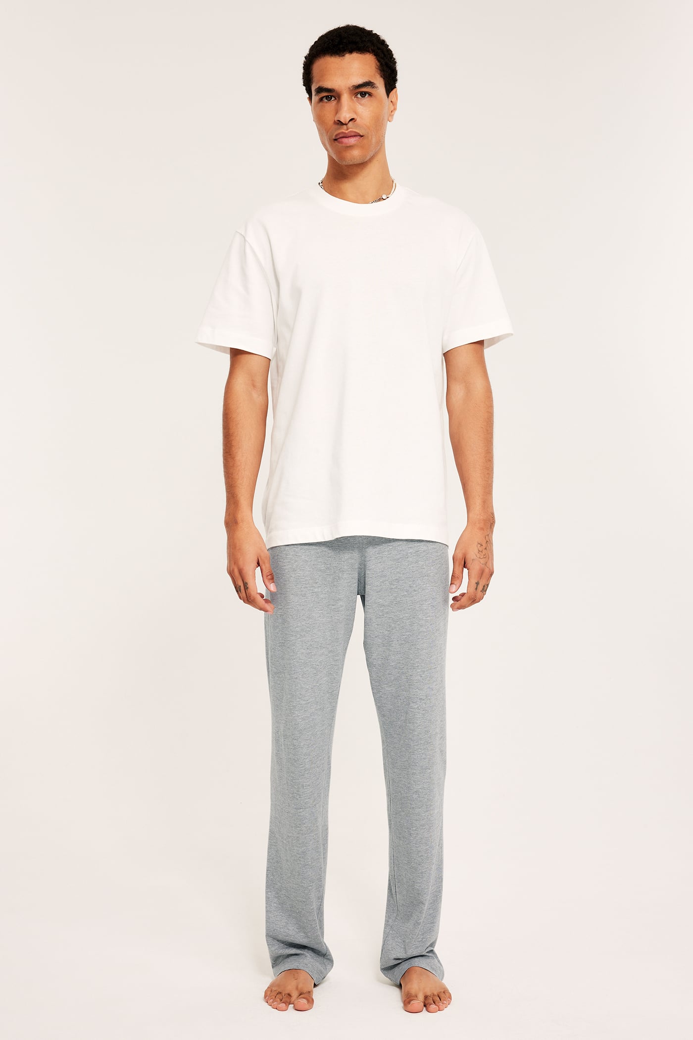 Man i vit T-shirt och ljusgrå pyjamasbyxor med melerat mönster, frontvy.