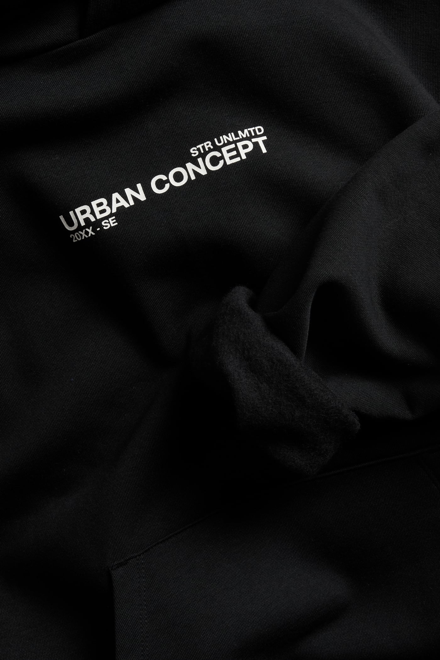 Zbliżenie na czarną bluzę z kapturem z białym nadrukiem „STR UNLMTD” i „URBAN CONCEPT”.