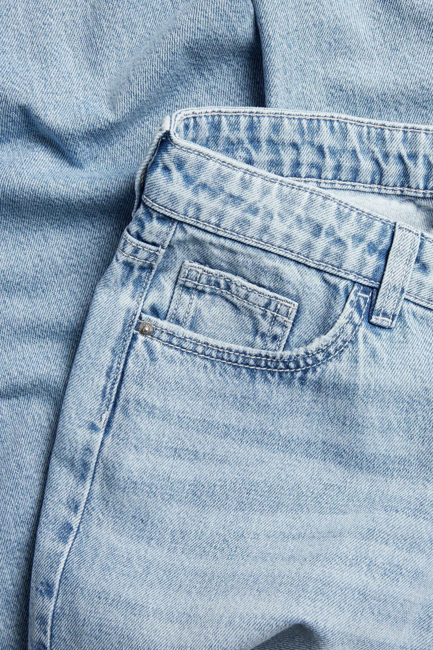 Lähikuva vaaleansinisistä denim-farkuista etutaskulla ja niitillä.