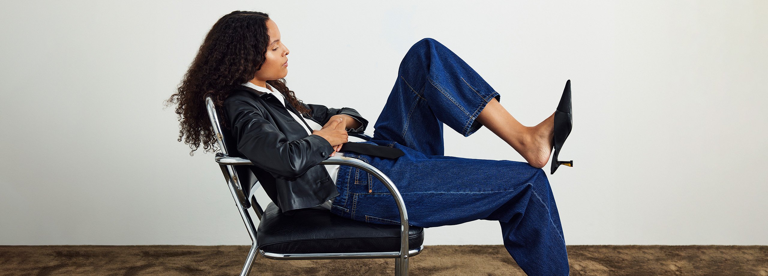 Kvinna sittandes på en läderstol i blå jeans och svart läderjacka.