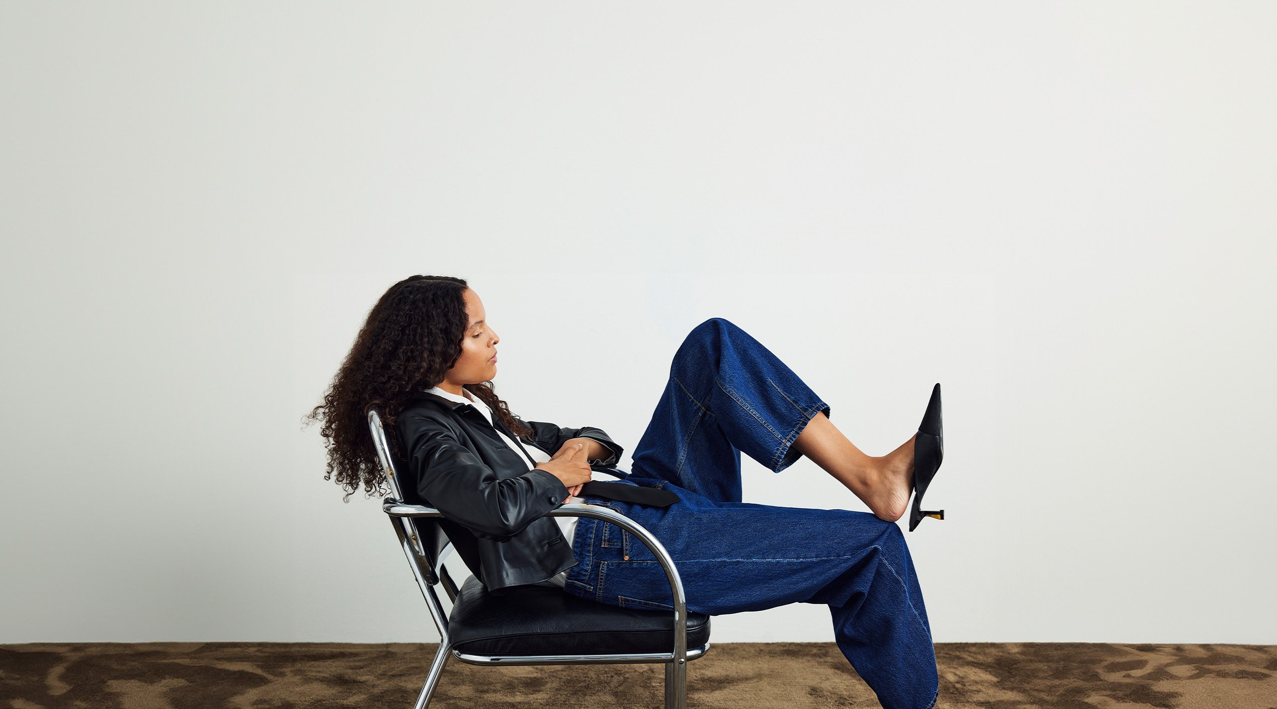 Kobieta siedząca na skórzanym fotelu w niebieskich dżinsach i czarnej skórzanej kurtce.