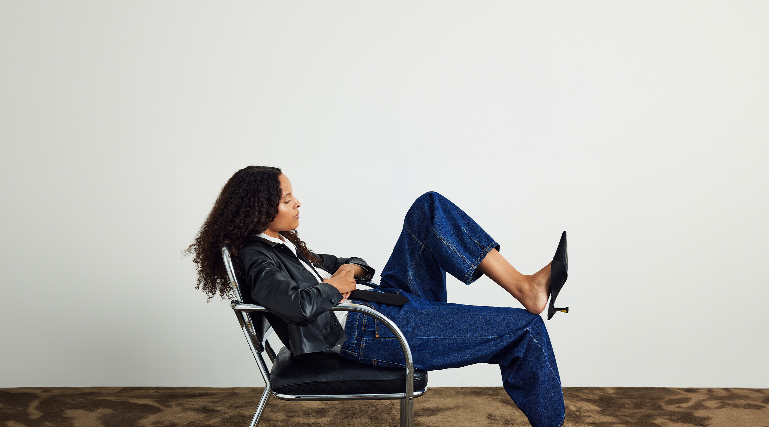 Kobieta siedząca na skórzanym fotelu w niebieskich dżinsach i czarnej skórzanej kurtce.