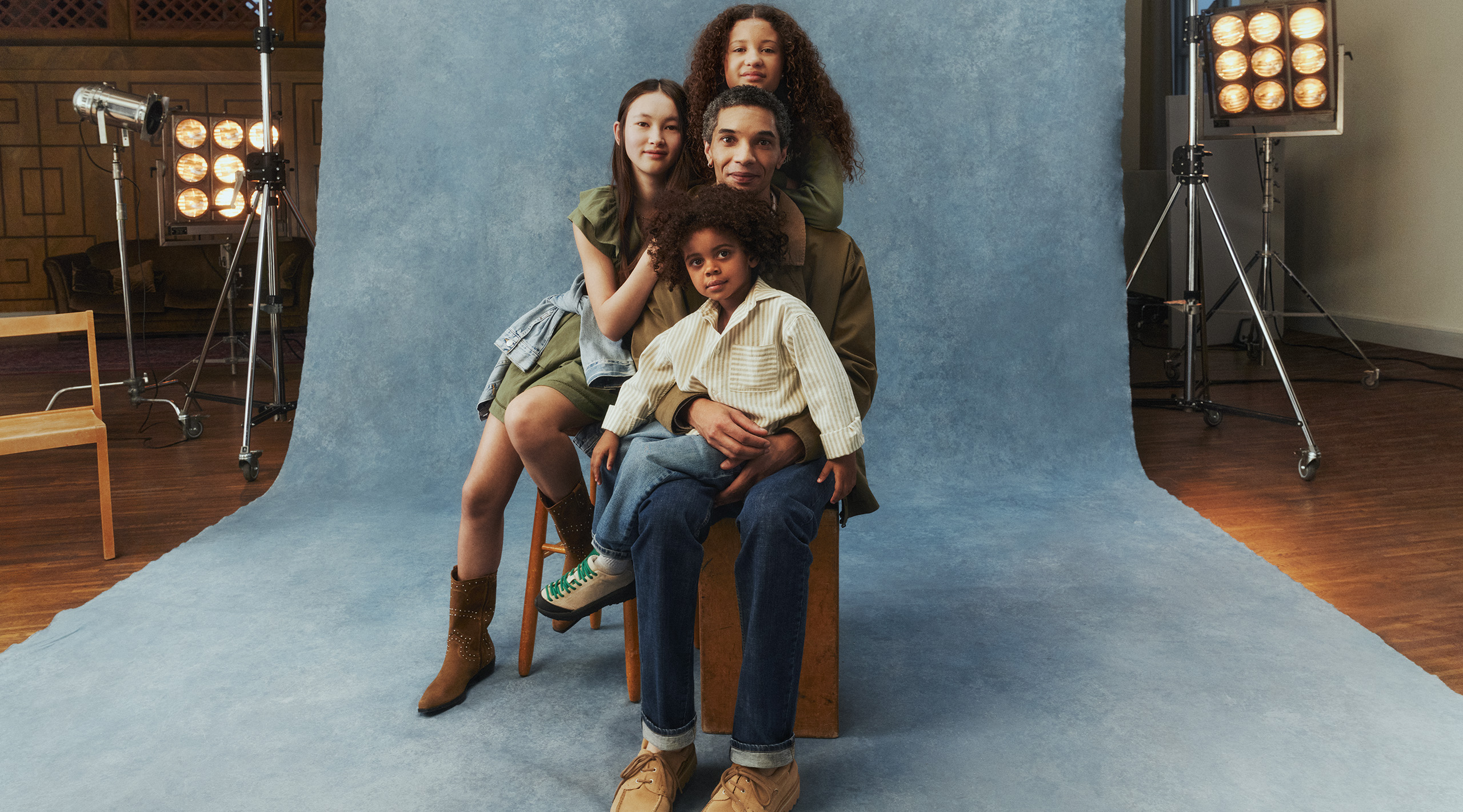 Mężczyzna otoczony trójką dzieci. Ma na sobie zieloną kurtkę i dżinsy. 