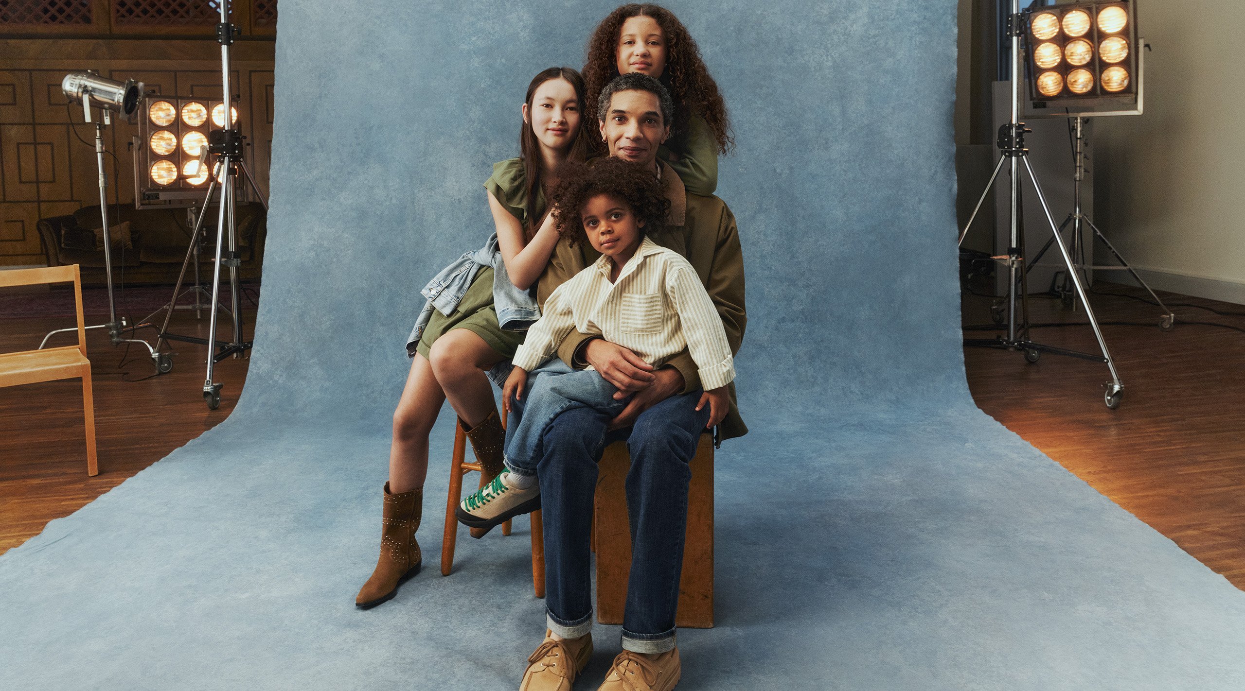 Mężczyzna otoczony trójką dzieci. Ma na sobie zieloną kurtkę i dżinsy.