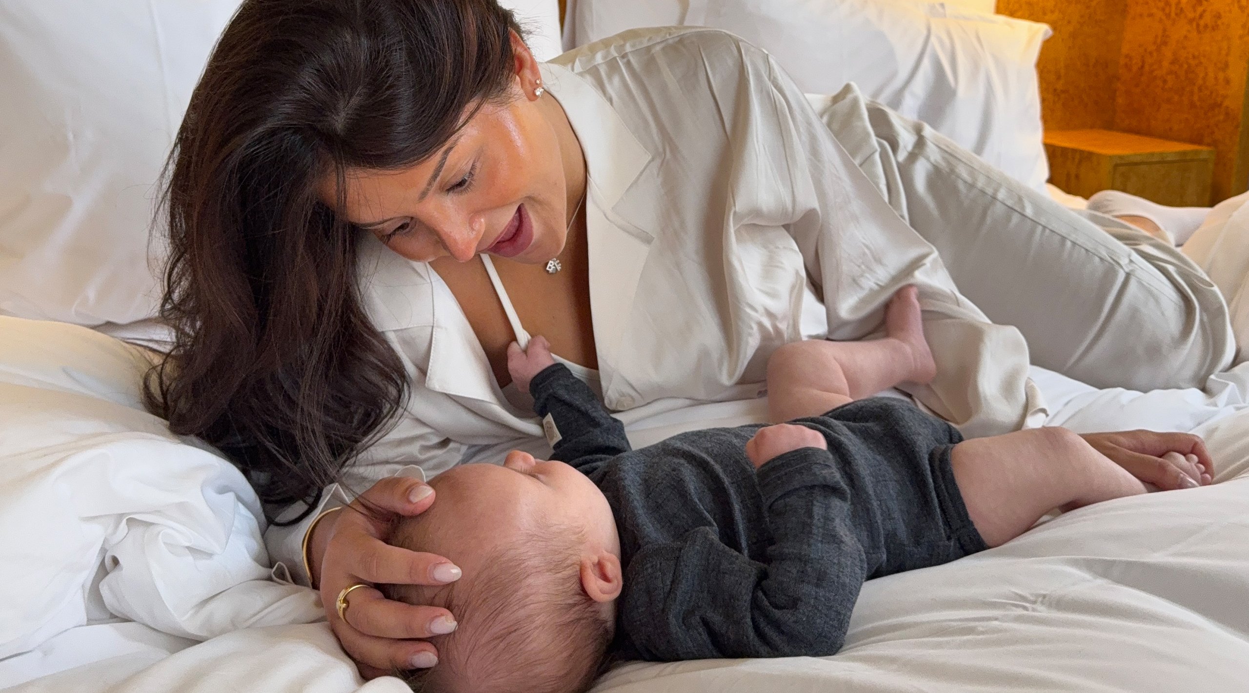 Mamma och bebis ligger i sängen och gosar klädda i kläder från Kappahl.