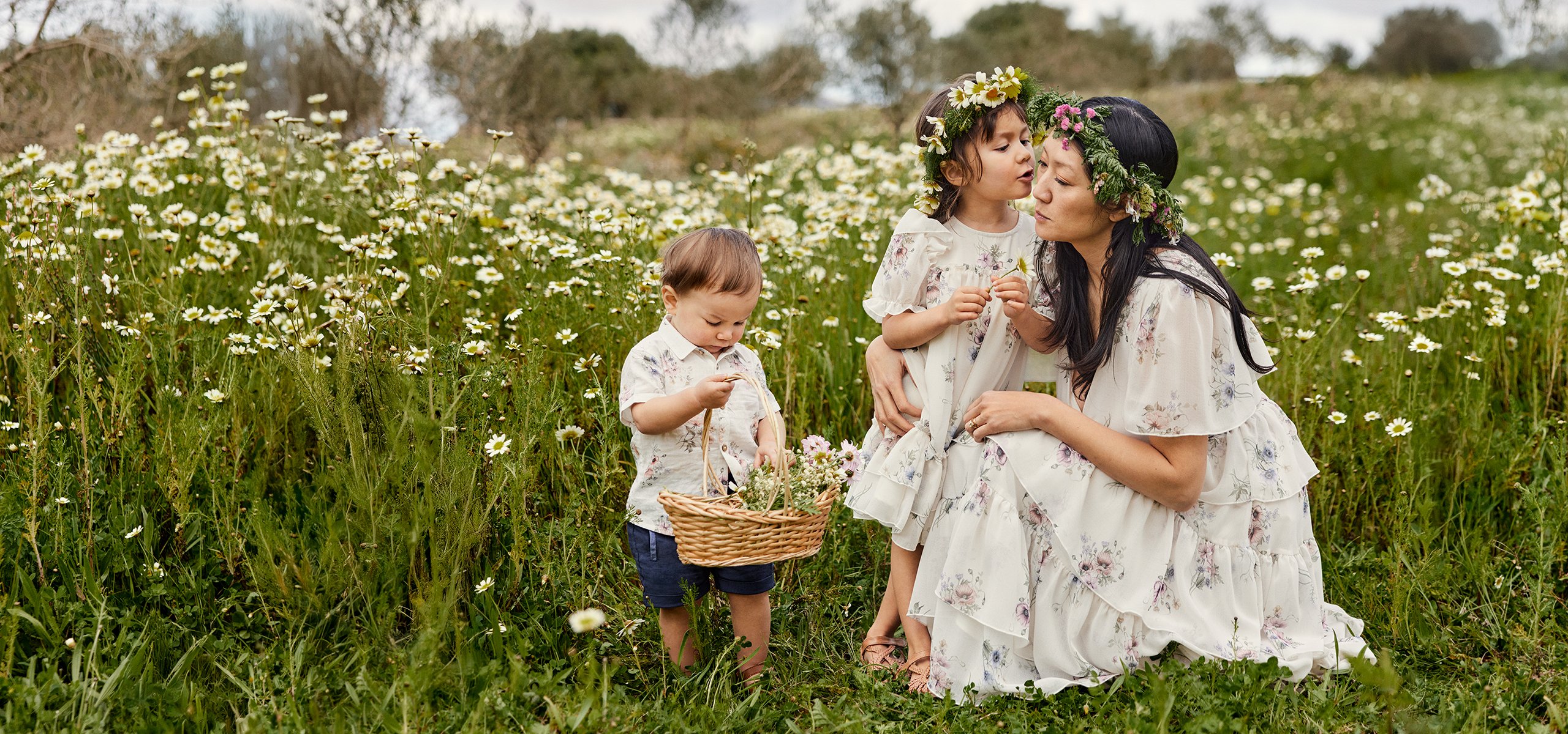 Barn och mamma lekandes vid blommorna i kläder från Newbie.