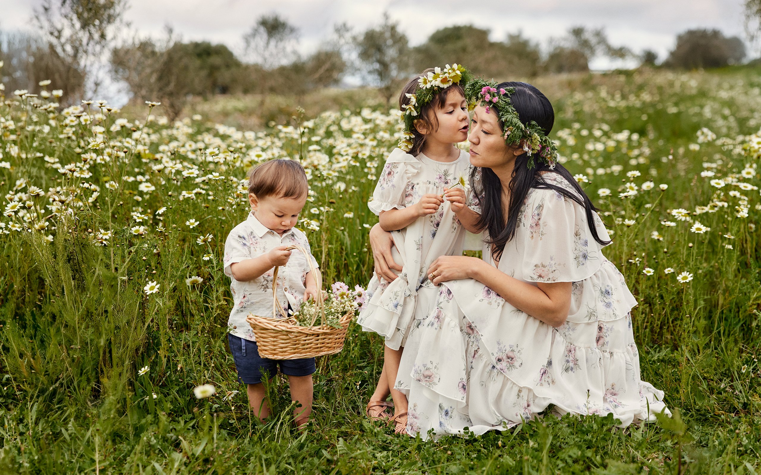 Mama z dziećmi bawiąca się wśród kwiatów w ubraniach od Newbie.