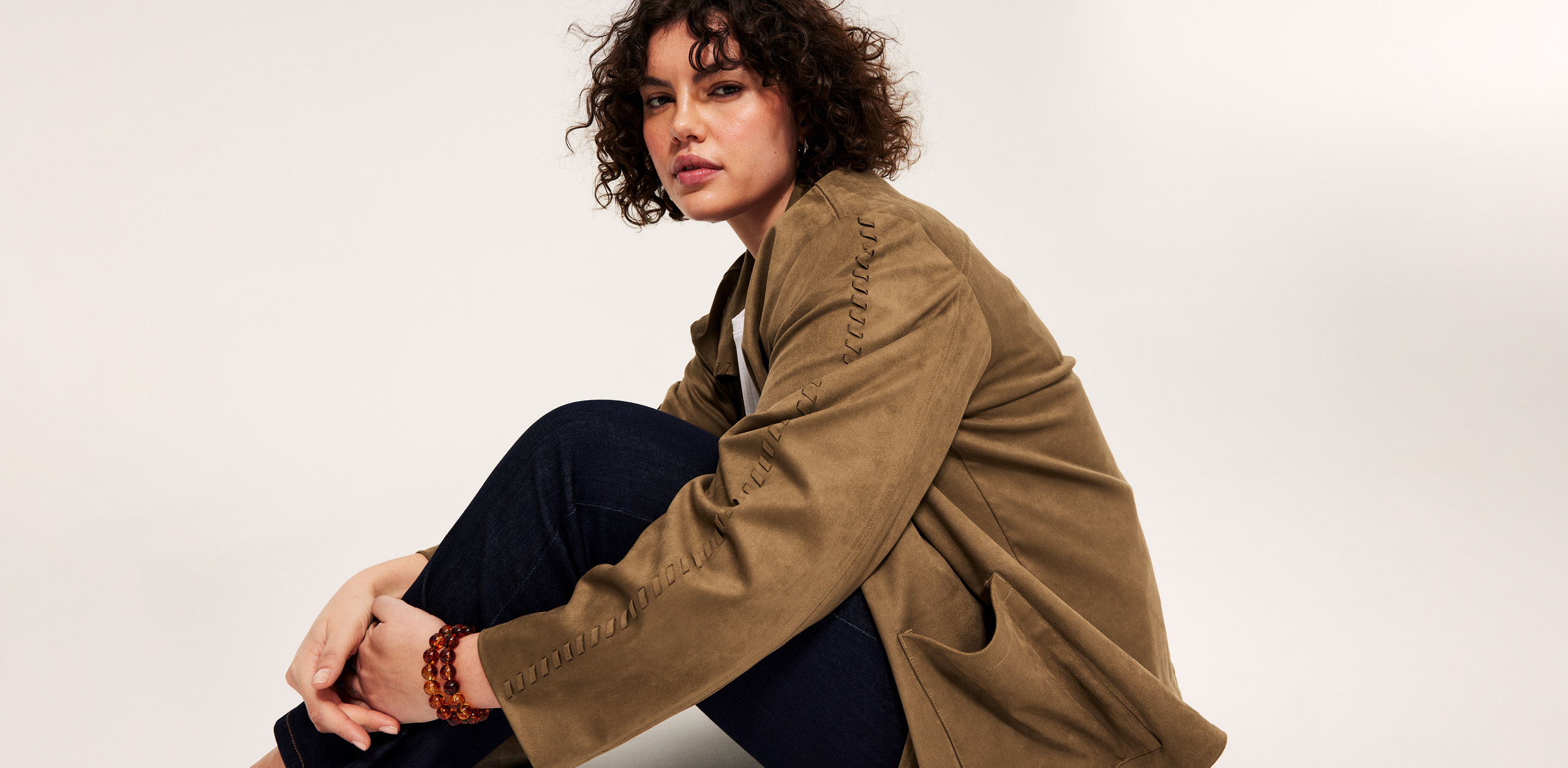 Nainen, plus size, istuu mokkanahkatakissa ja farkuissa. 