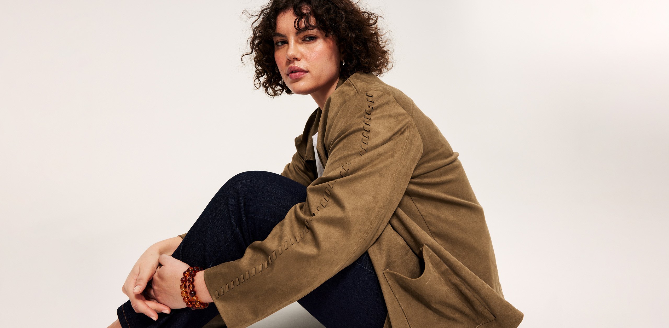 Nainen, plus size, istuu mokkanahkatakissa ja farkuissa.