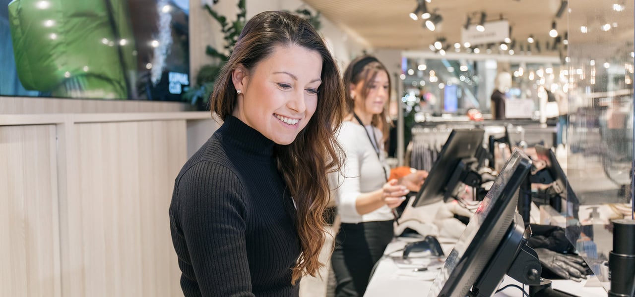 Smiling store employee behind the counter in a Kappahl store.
