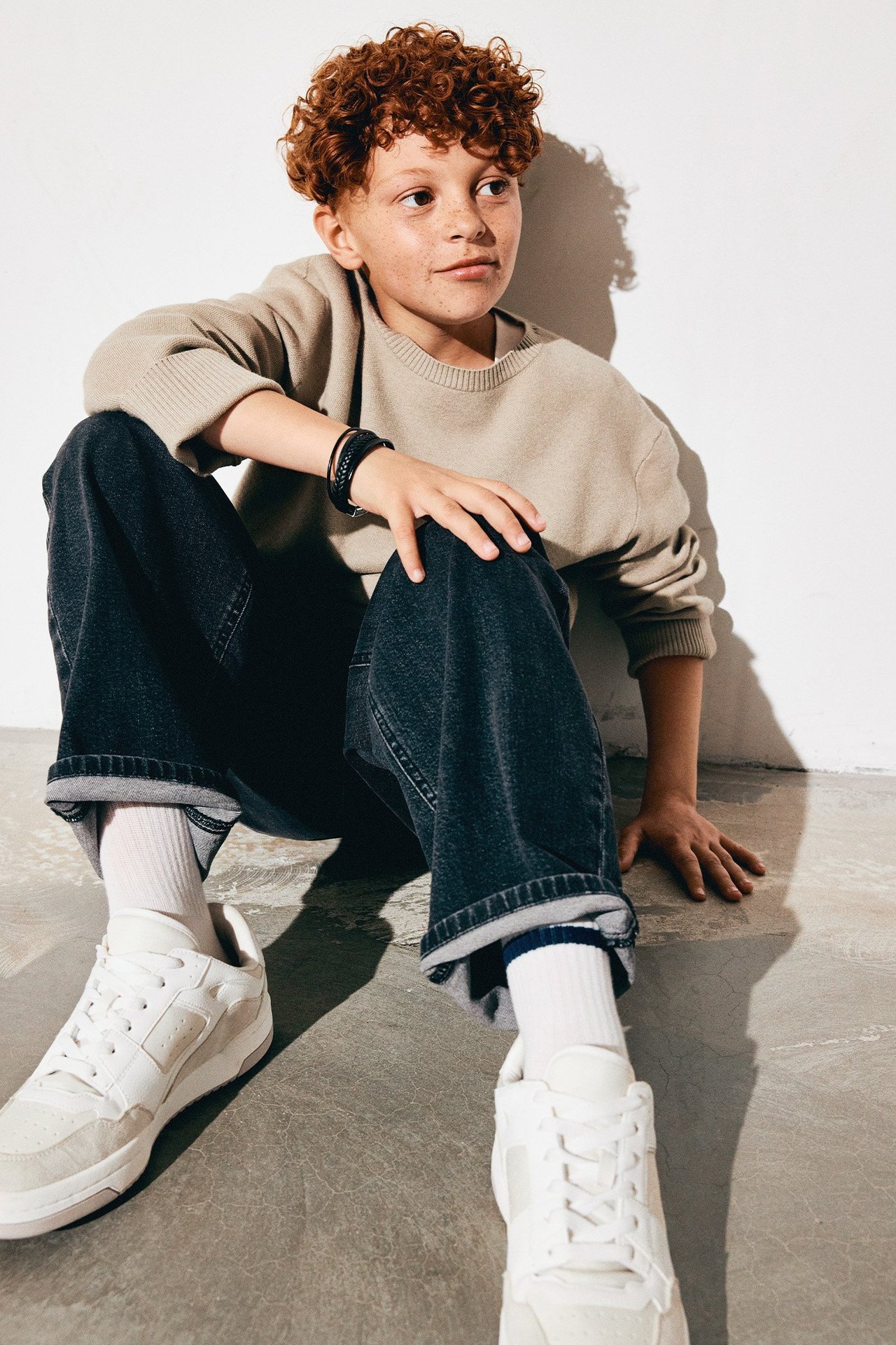 Kille i jeans och stickad tröja sittandes på ett stengolv.