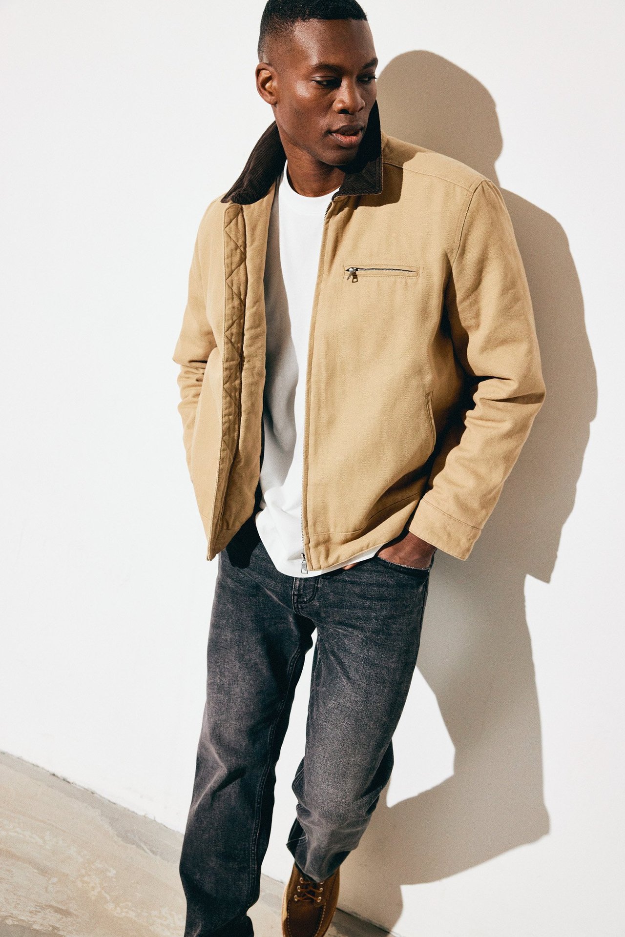 Man i grå jeans, vit t-shirt och workwear-jacka.