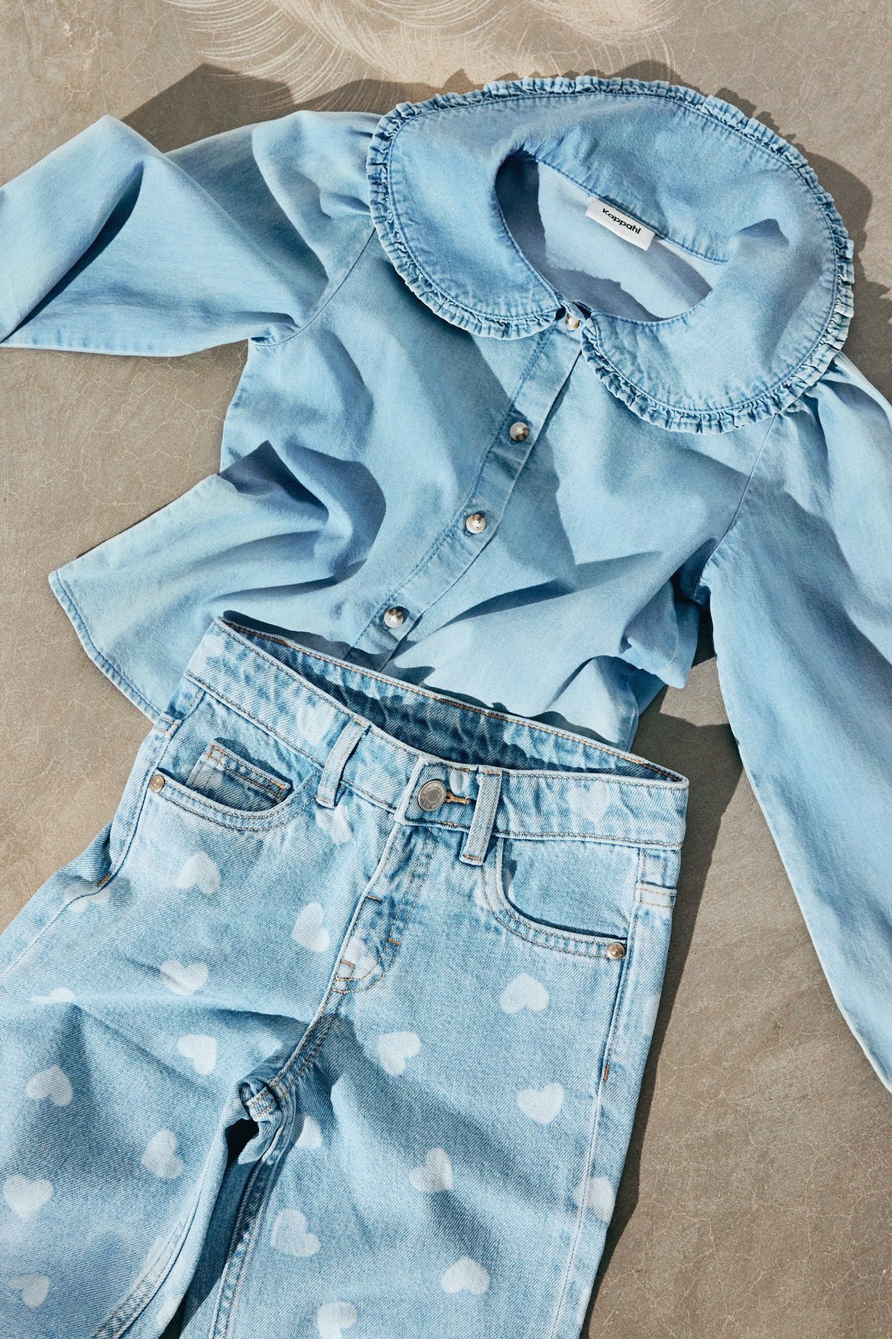 En jeansblus och ett par jeans med hjärtan på liggandes på ett stengolv.