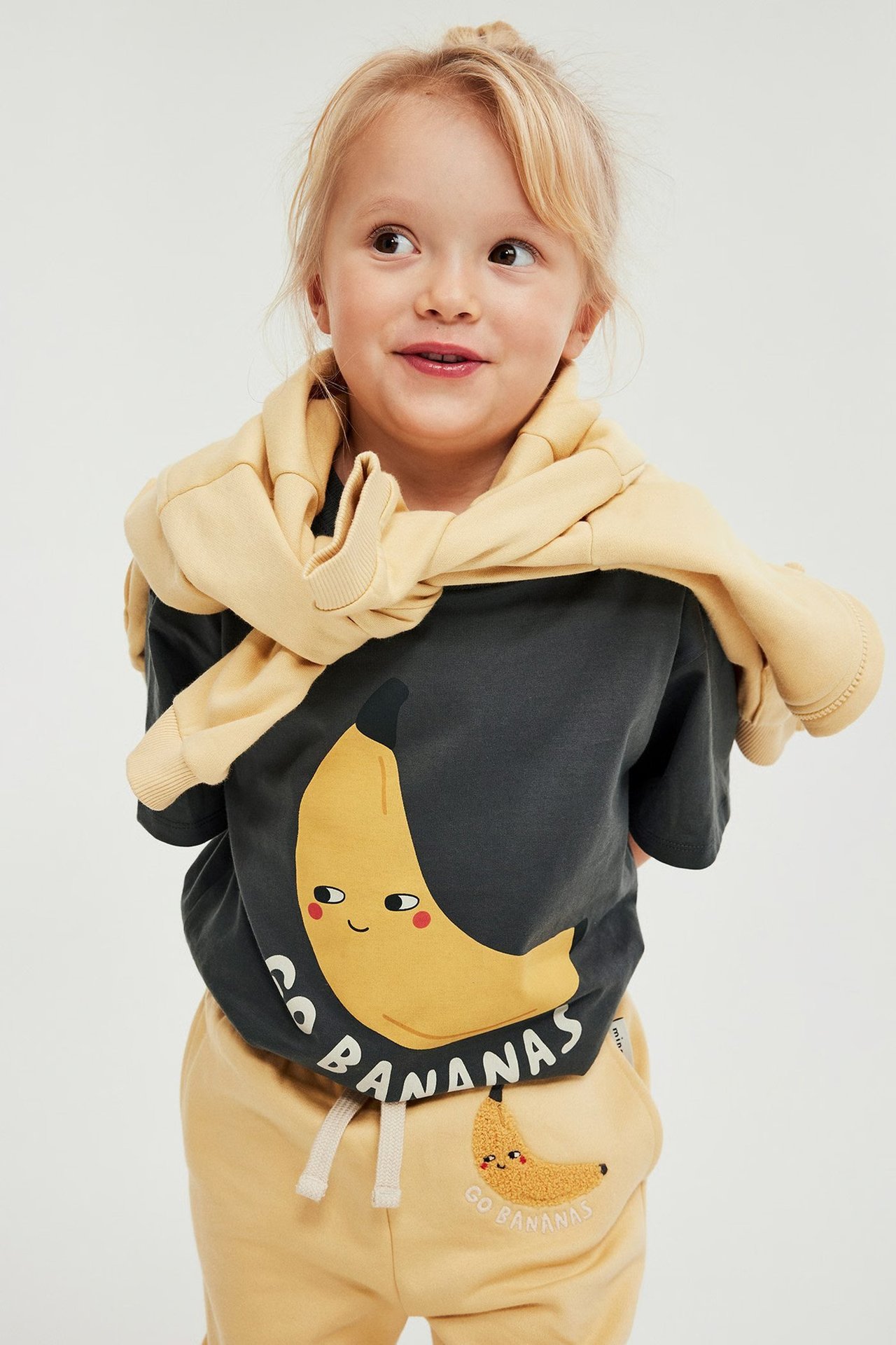 Dziecko w żółtych ubraniach z bananami.