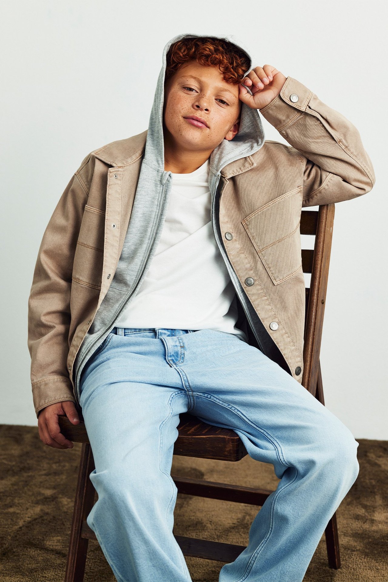 Facet siedzi na krześle w jasnoniebieskich dżinsach i beżowej koszuli.