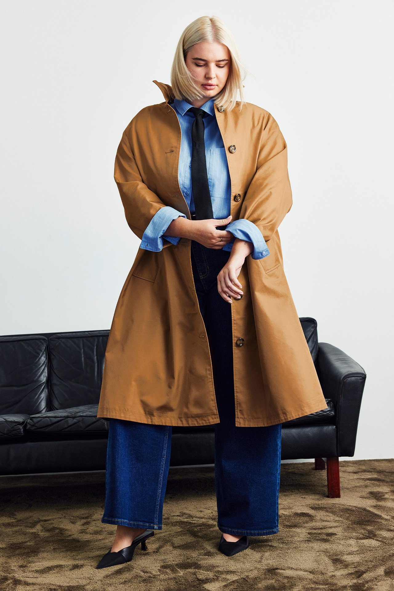 Kobieta ubrana w płaszcz przeciwdeczny, koszulę, krawat i dżinsy.