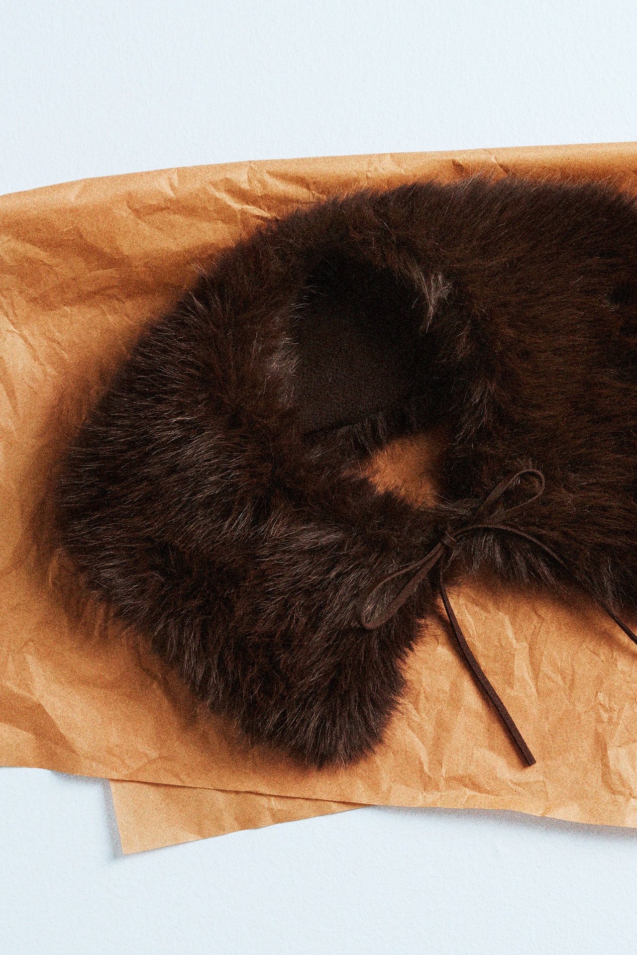 Futrzany kołnierz z imitacji futra, leżący na brązowym papierze prezentowym.