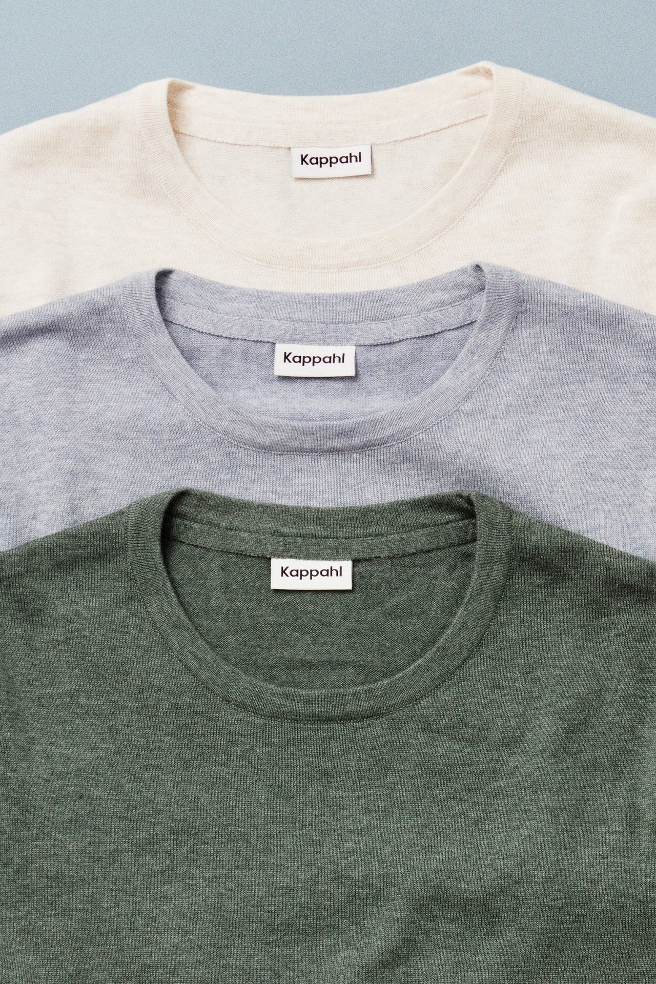 Trzy dzianinowe swetry męskie sfotografowane na niebieskim tle