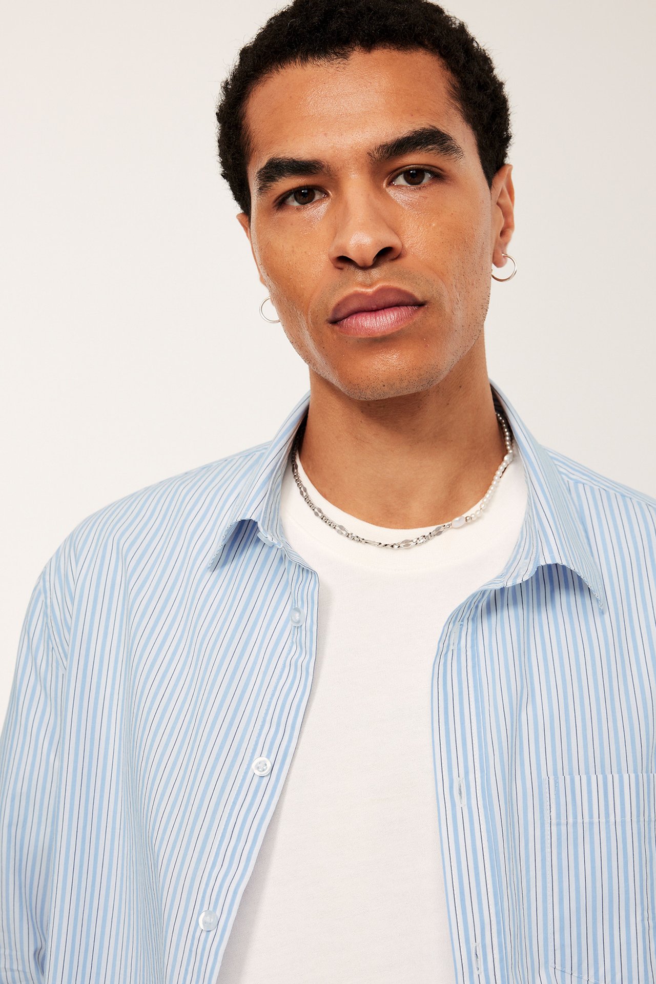 Blå og hvit stripete herreskjorte med hvit T-skjorte under. Fotografert mot betonggulv. 