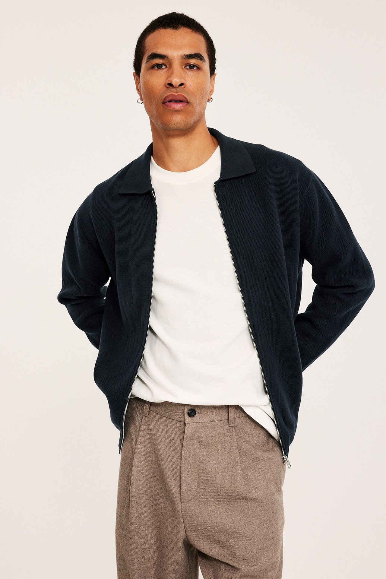 Tre strikkede herre-gensere fotografert mot en blå bakgrunn