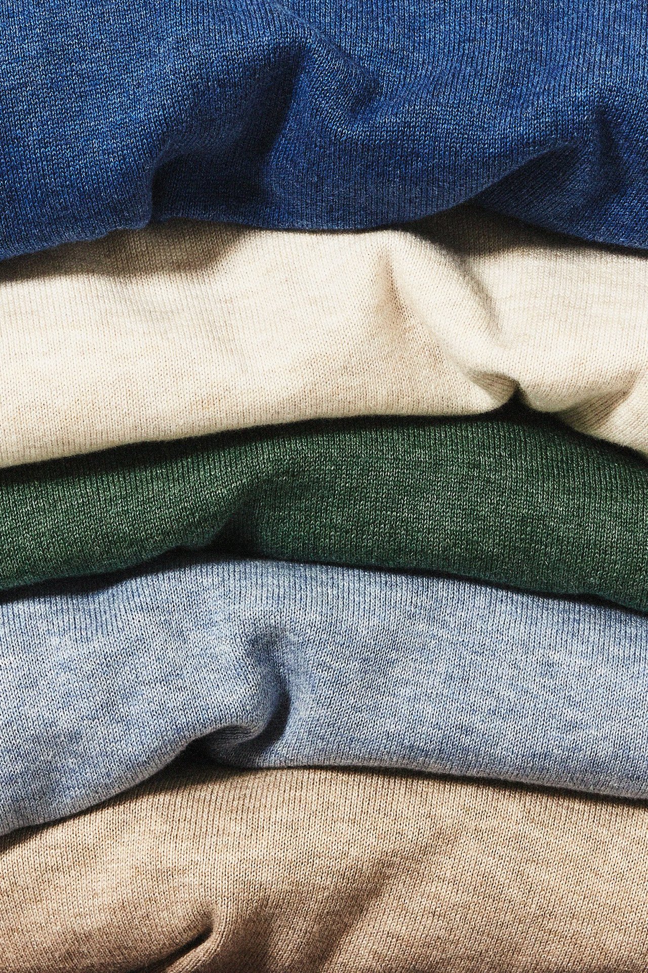 Lähikuva viisi neulottuja villapaitoja väreissä sininen, beige, vihreä ja ruskea. 