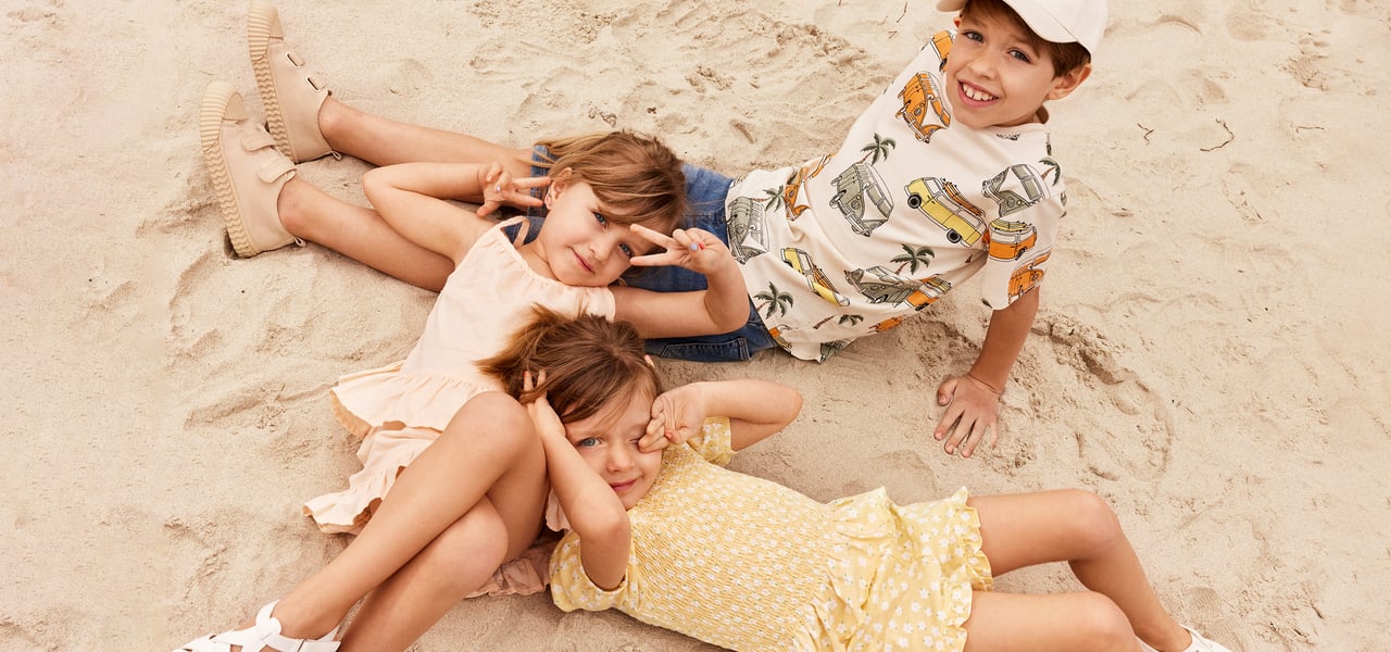 Barn på en strand med sommarkläder.