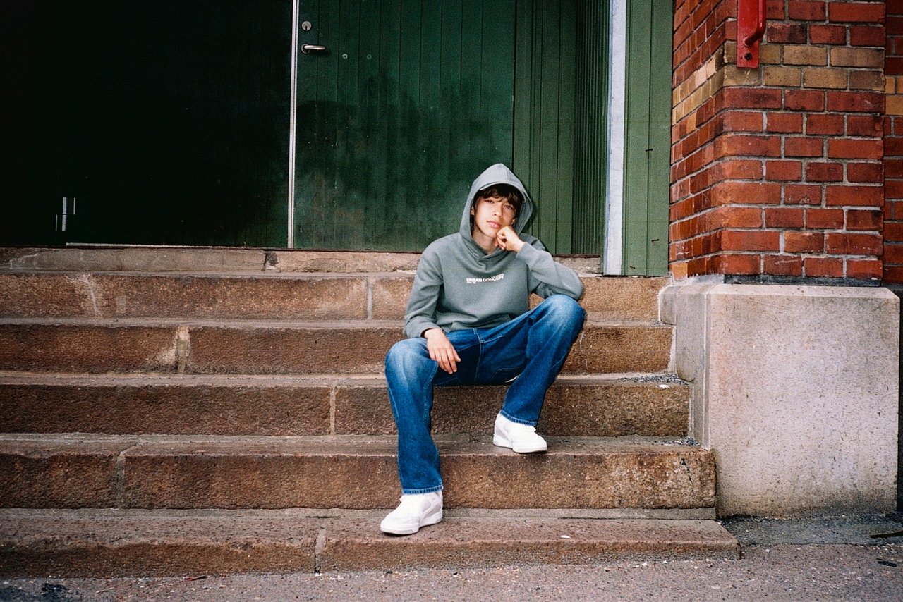 En kille sittandes i en trappa med blå jeans och grön hoodie.