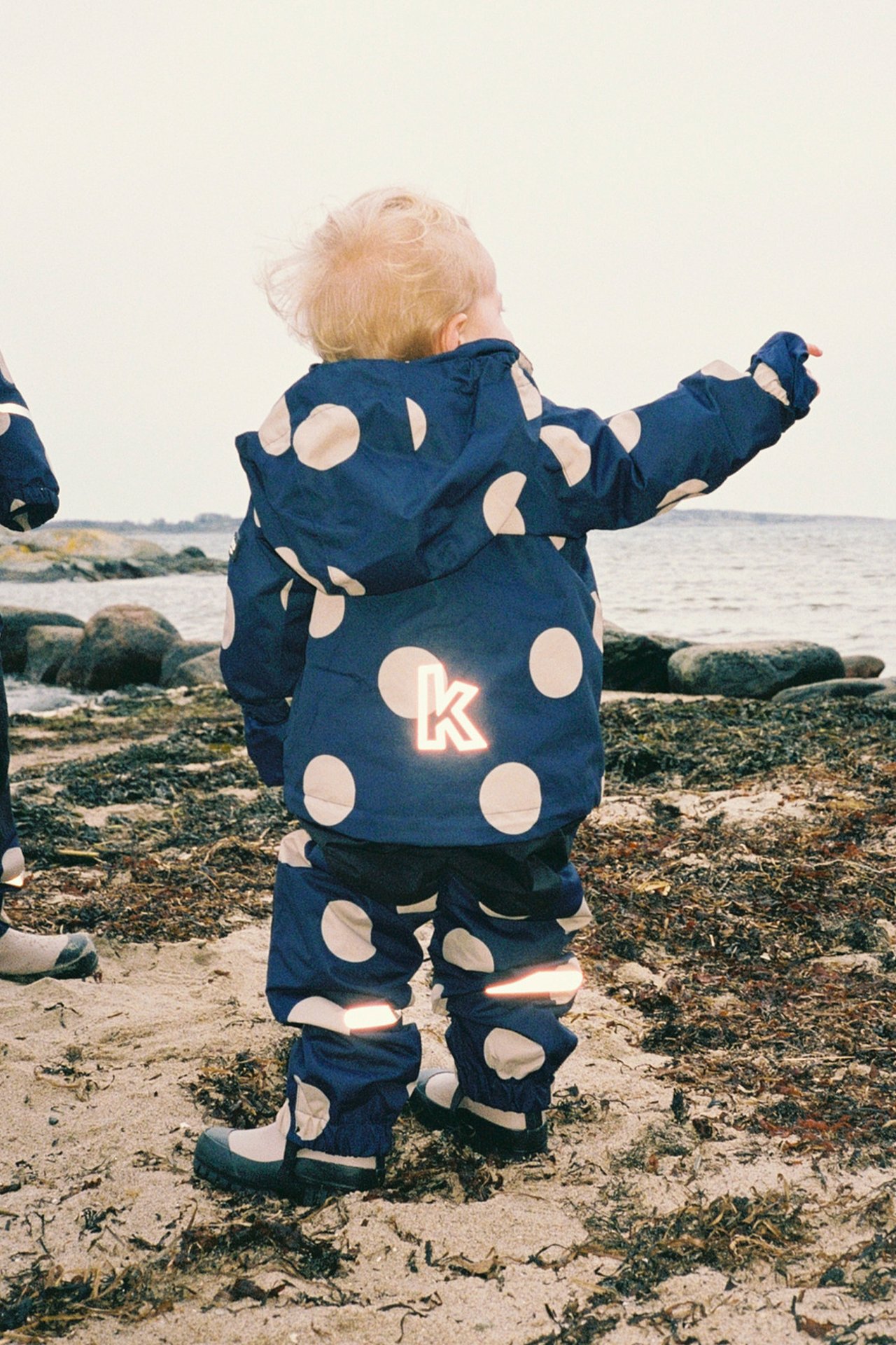 Lapset meren rannalla vuoratuissa sadevaatteissa.