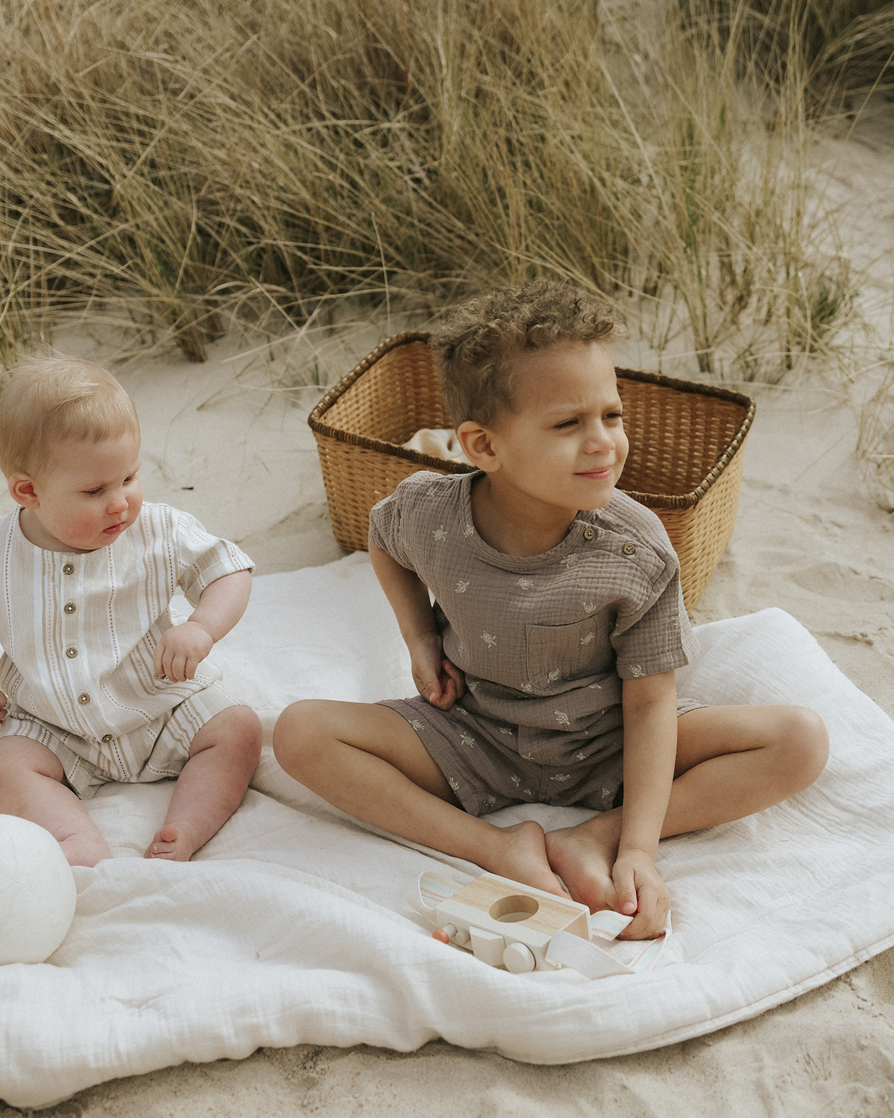 Chłopcy siedzą na kocu na plaży z ładnymi ubraniami od Newbie
