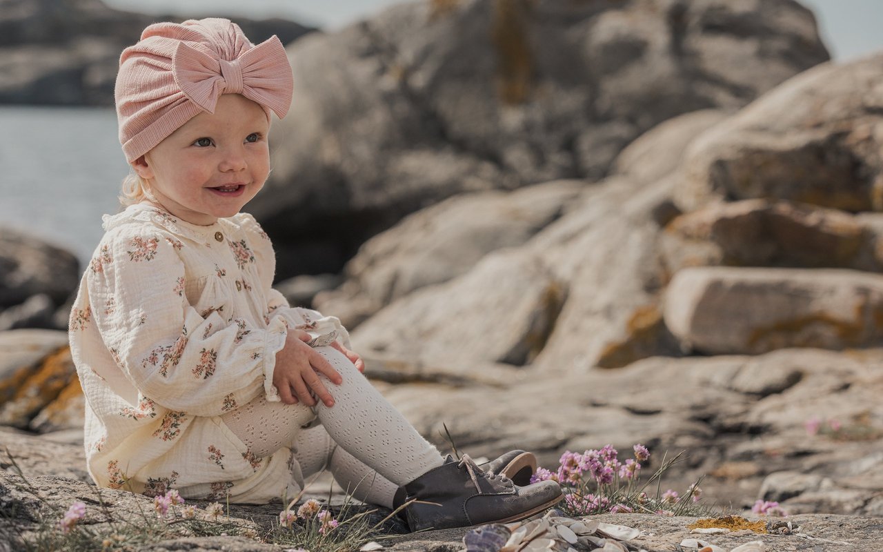 Liten jente kledd i lue, kjole og strømpebukser fra Newbie.