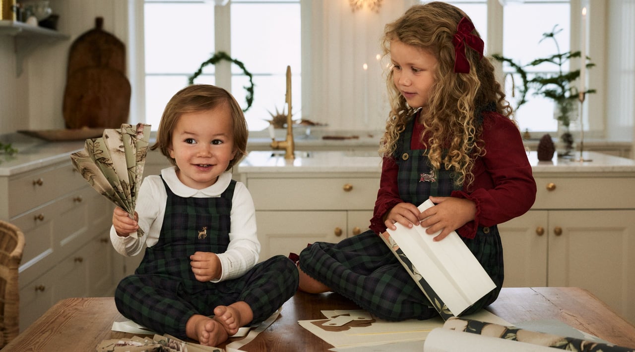 Dziewczynka i chłopiec bawią się w kuchni, ubrani w świąteczne ubrania od Newbie.