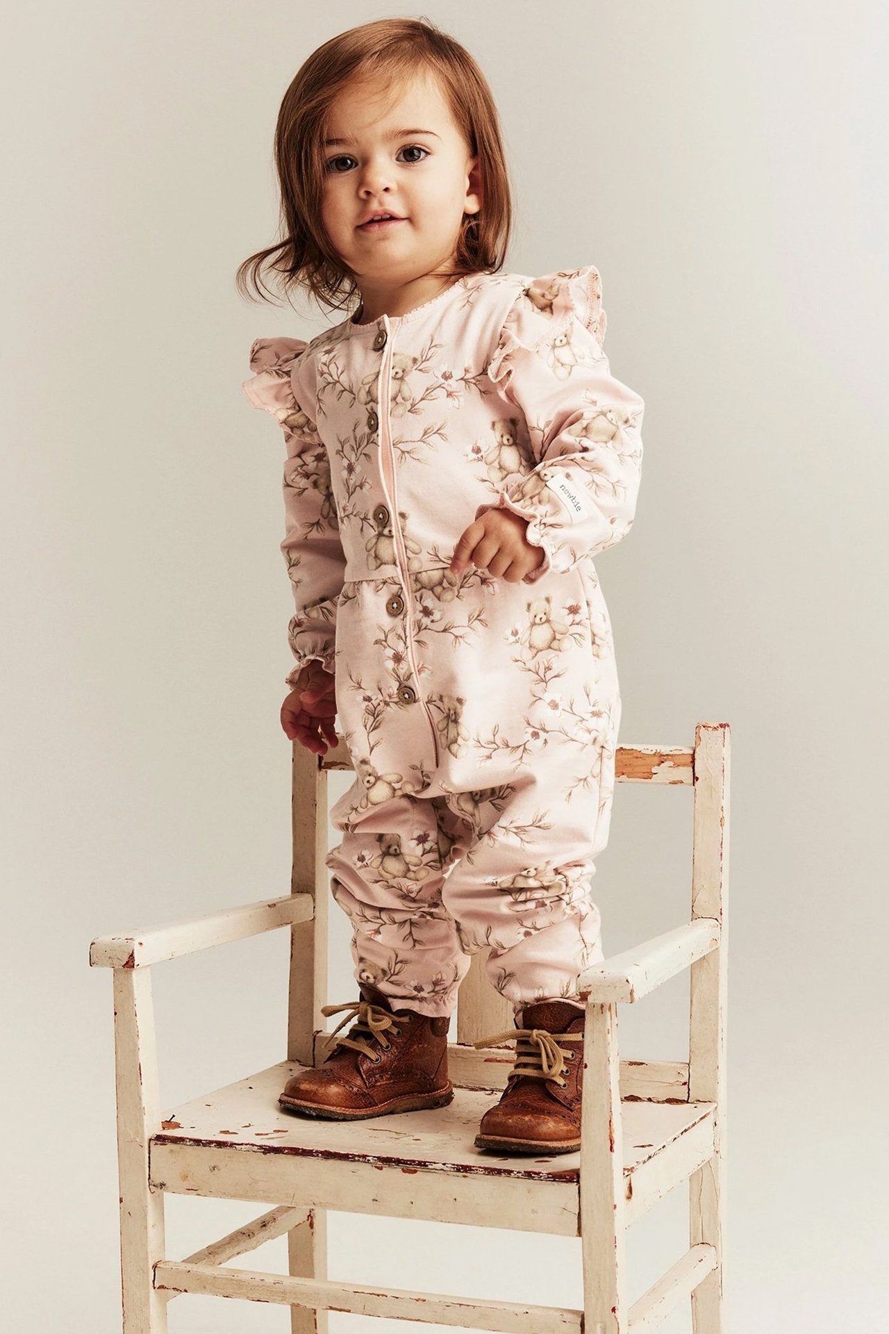 Dzieci ubrane w kwieciste kombinezony od Newbie, stojące na krześle.