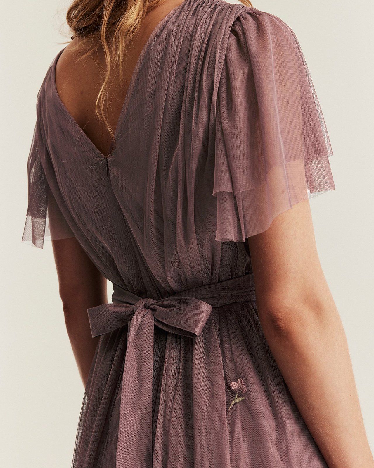 Kobieta ubrana w fioletową siateczkową sukienkę z kokardą z tyłu w talii.