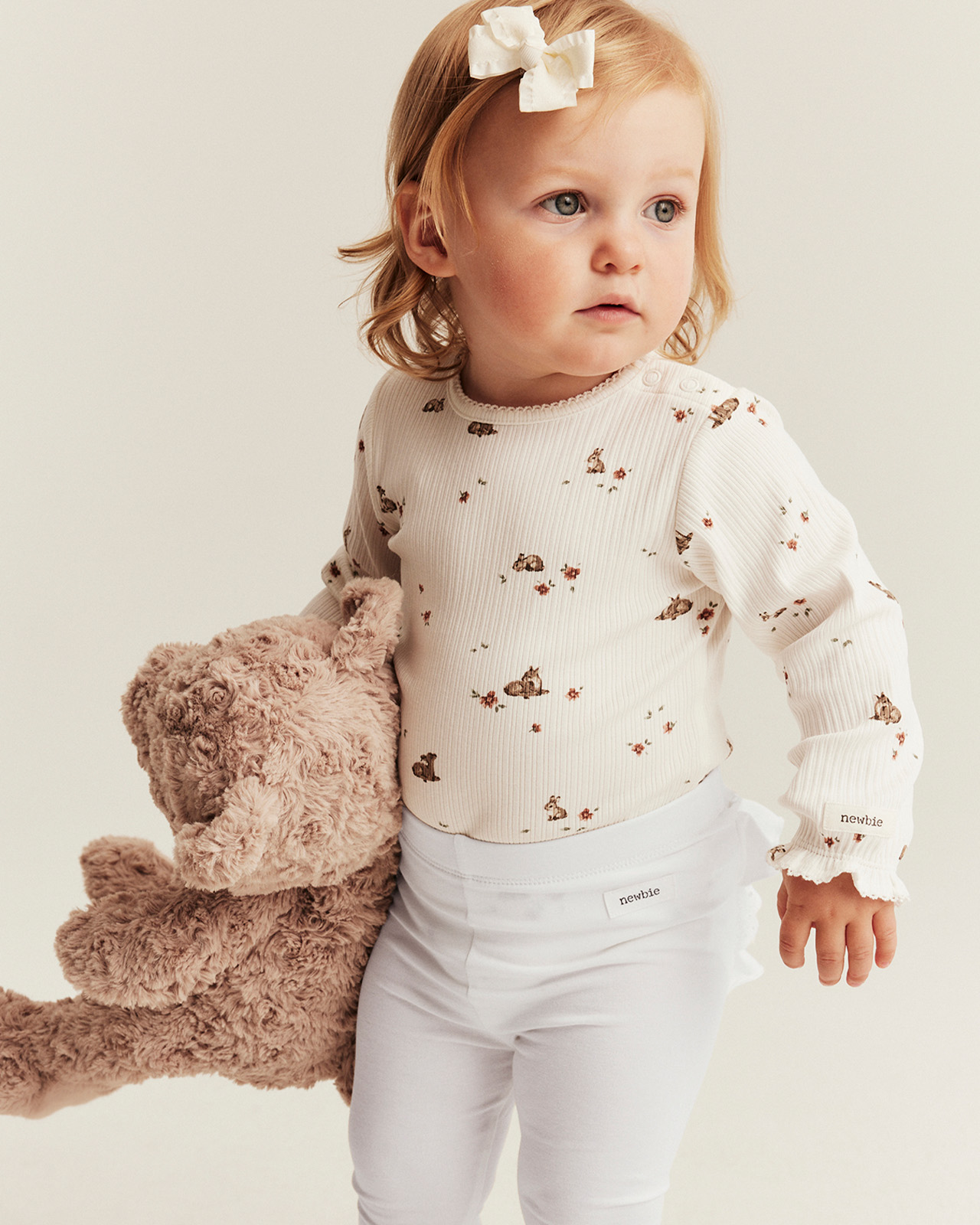 Liten tjej som bär på en nalle och har på sig en blommig topp