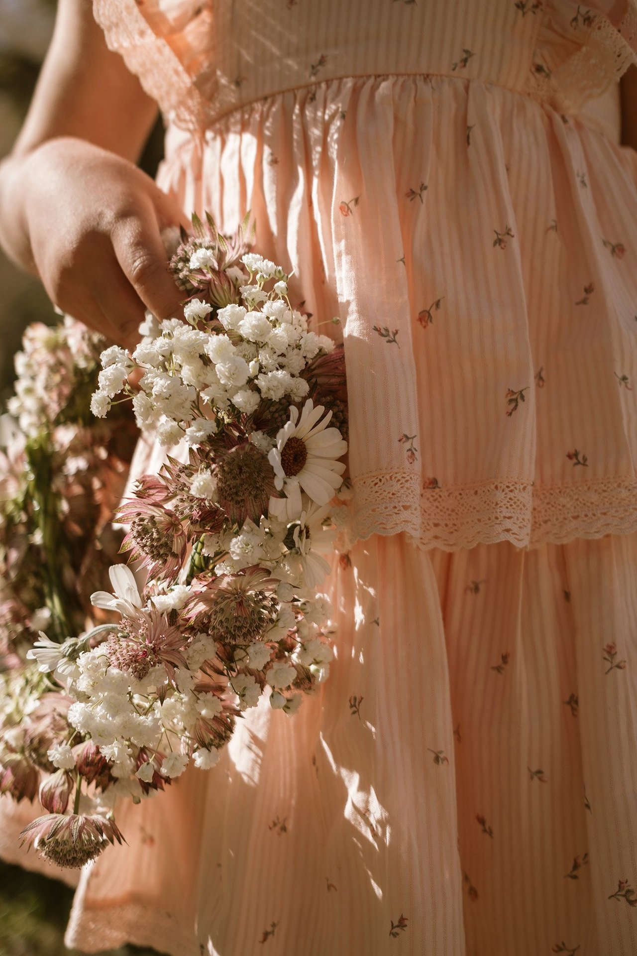 Close-up of a girl holding a handmade flower wreath while wearing a soft pink summer dress.