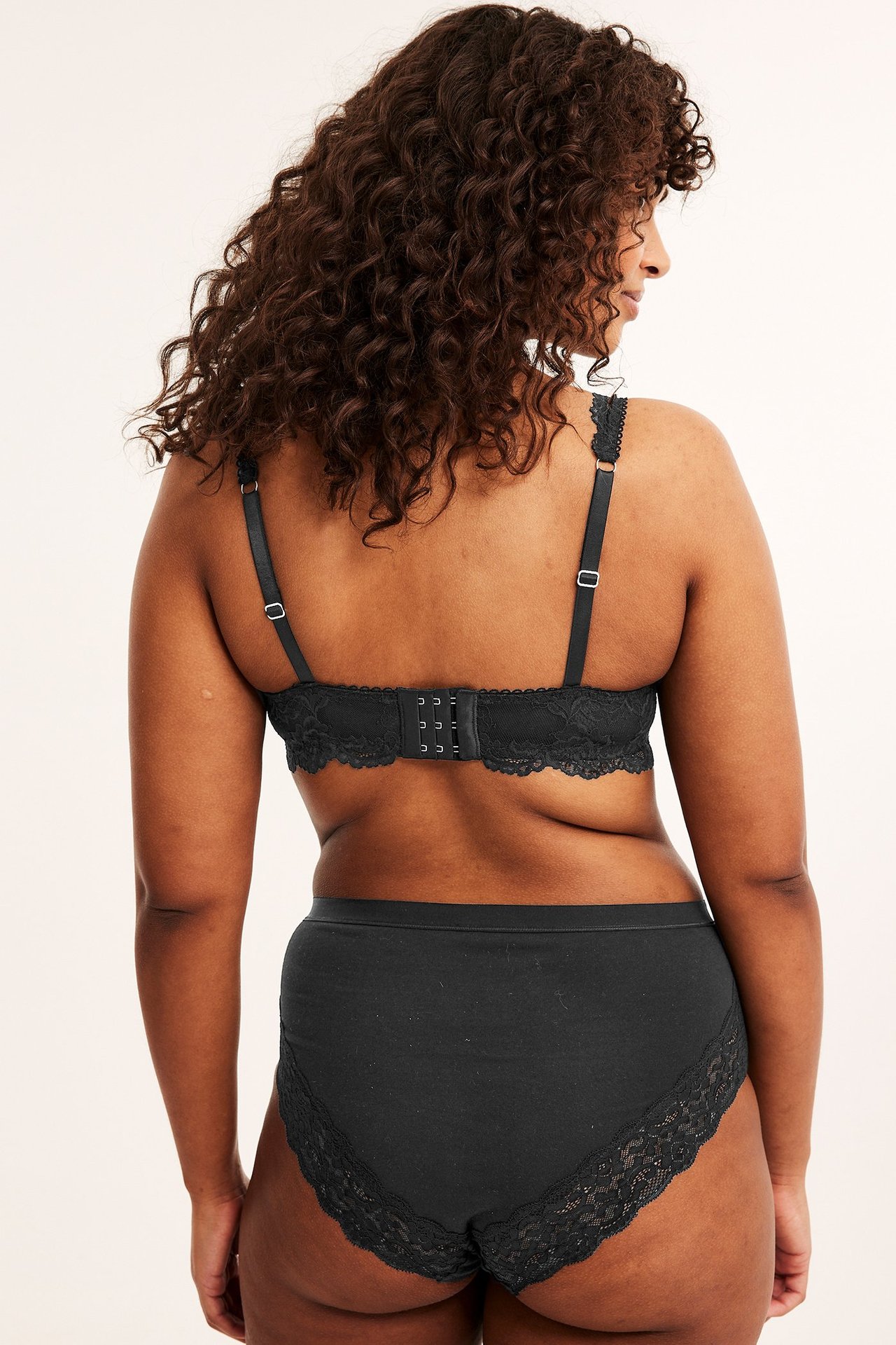 Ryggvy av en kvinna i svarta bomullstrosor med spetsdetaljer och matchande svart spetsbehå.