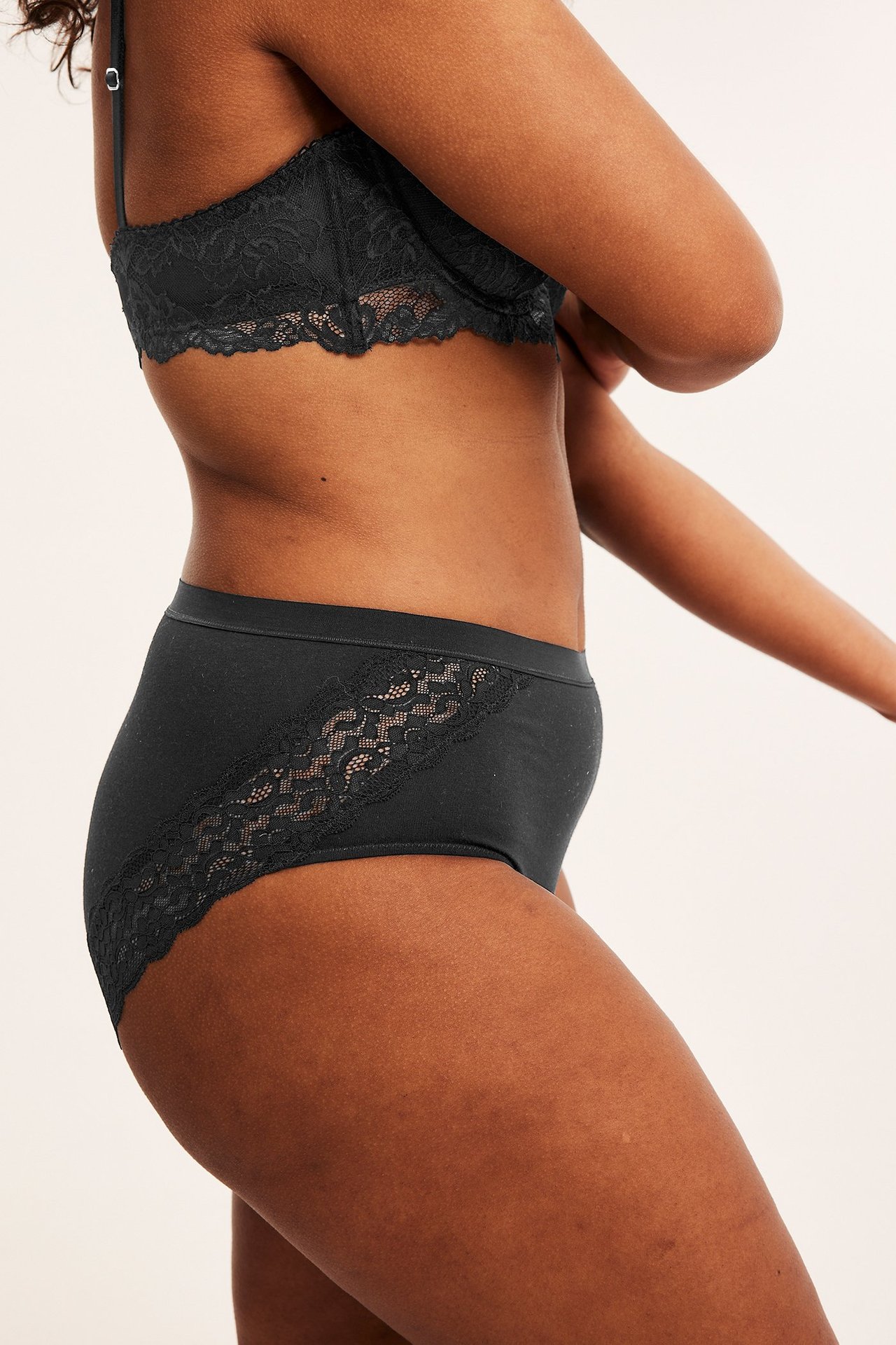 Sideutsikt av en kvinne i svarte bomullstruser med blondedetaljer og en matchende svart blonde-BH.