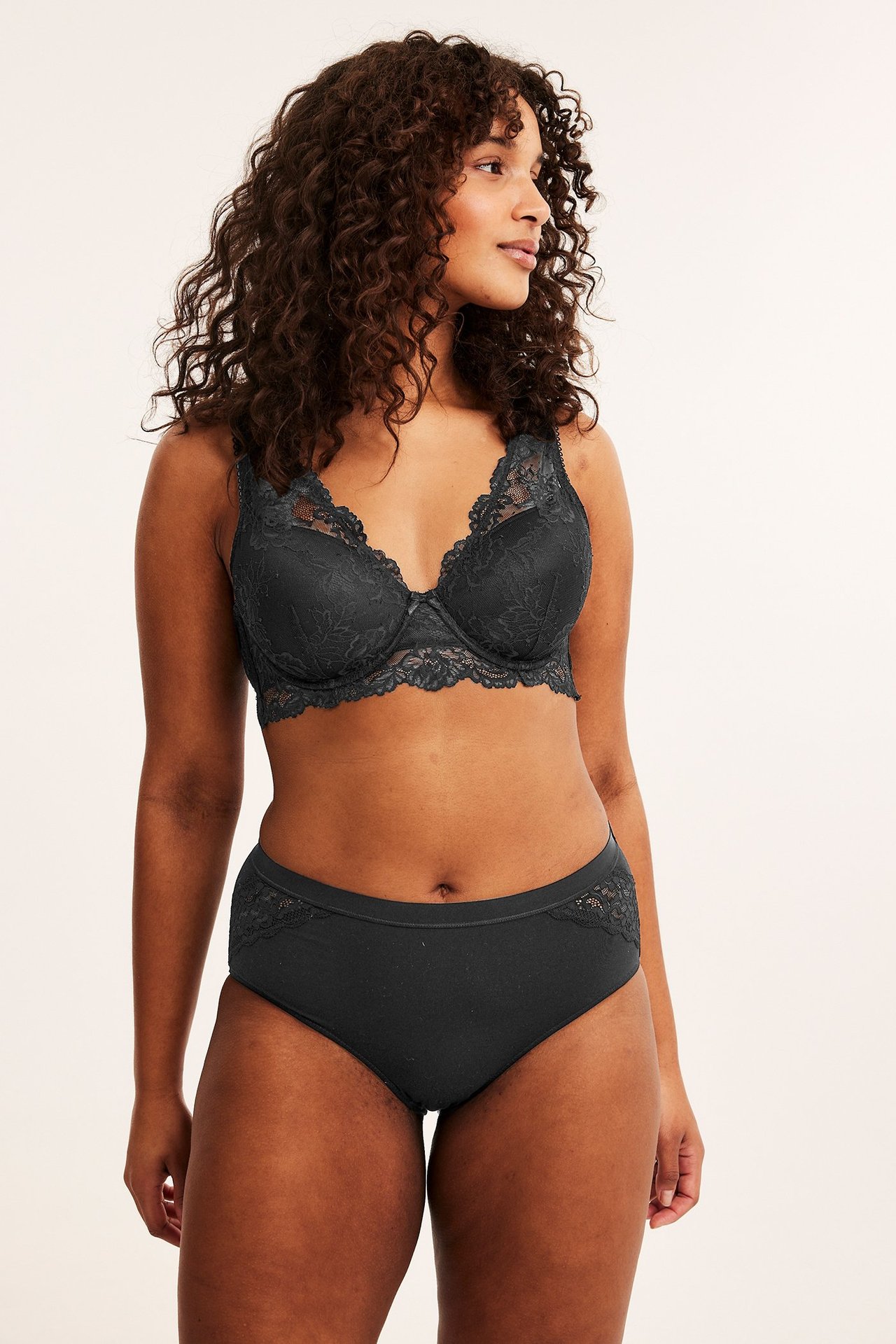 Forfra, kvinne iført svarte bomullstruser med blondedetaljer og en matchende svart blonde-BH.