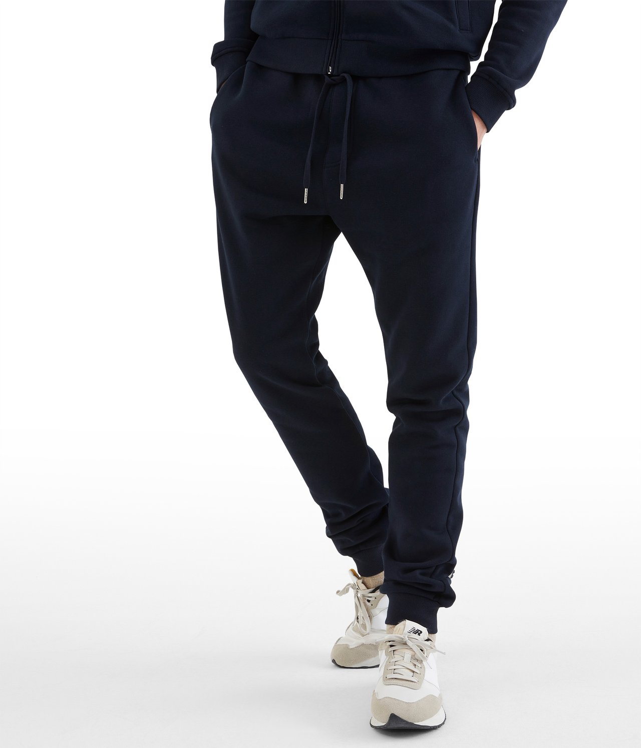 Widok z przodu: mężczyzna w ciemnoniebieskich dresach z mieszanki bawełny ze sznurkiem, kieszeniami, ściągaczami i sneakersach.