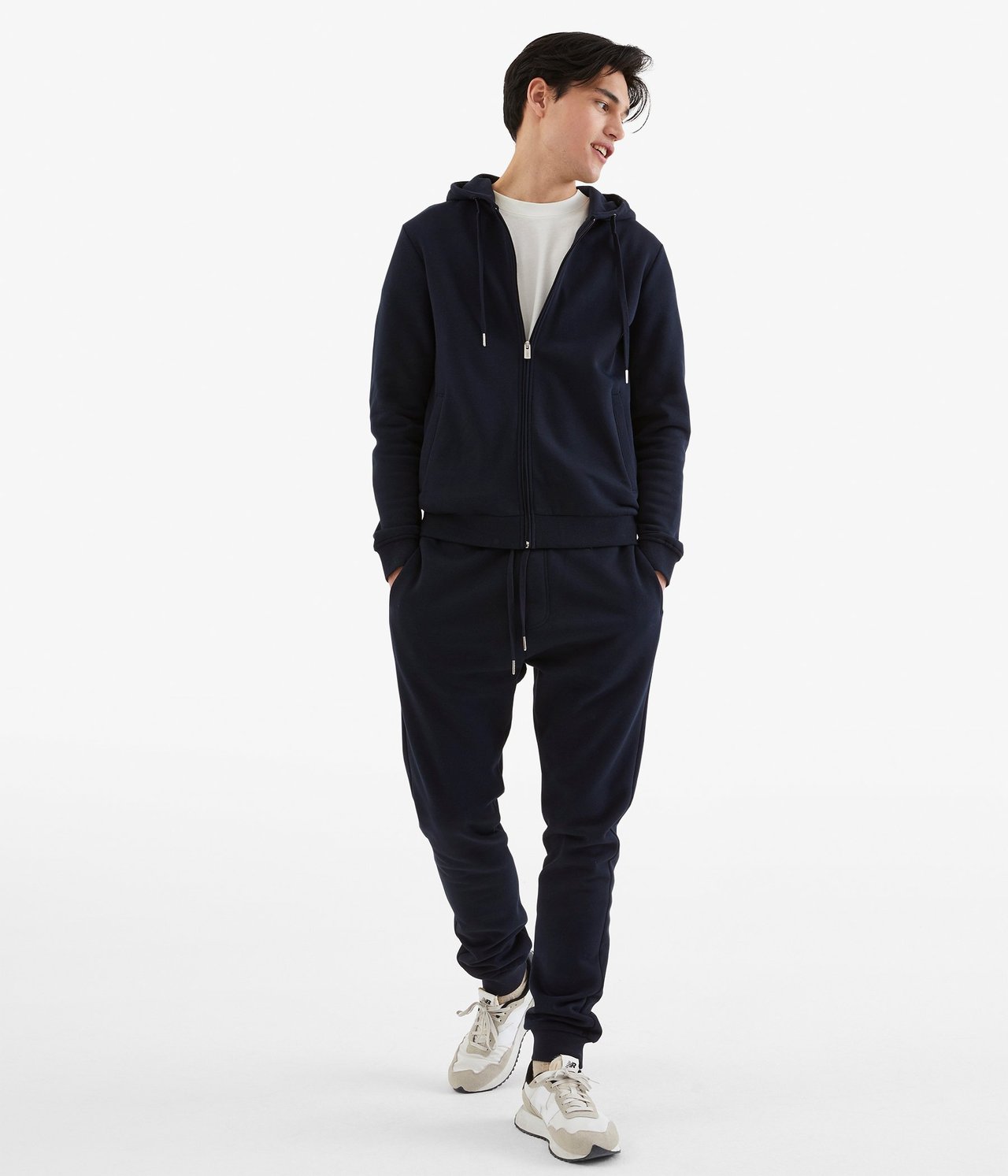 Widok z przodu: Mężczyzna w granatowych dresach ze ściągaczami, pasującej bluzie, białym t-shircie i trampkach.