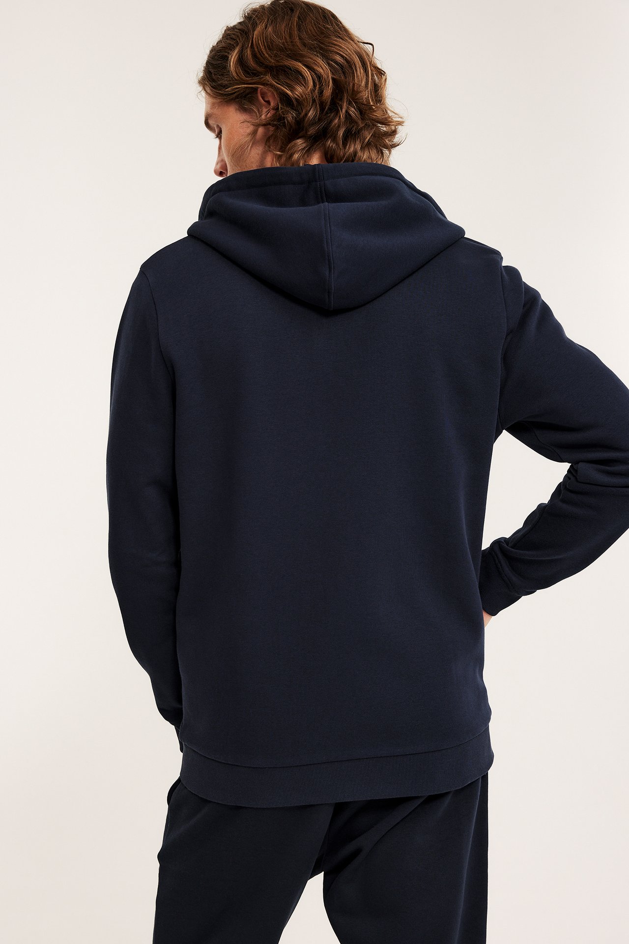 Miehen takakuva tummansinisessä vetoketjuhupparissa ja yhteensopivissa collegehousuissa.