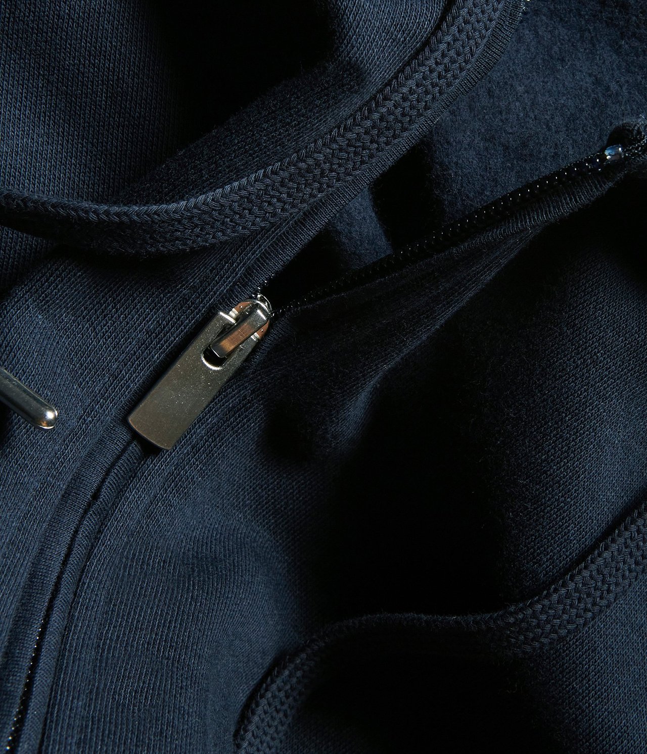 Zbliżenie na granatową bluzę z kapturem, z metalowym zamkiem błyskawicznym i sznurkiem.