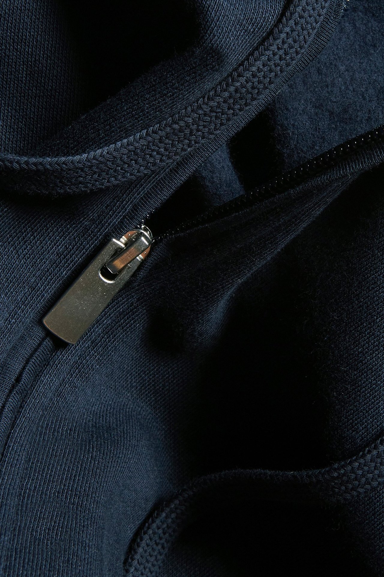 Zbliżenie na granatową bluzę z kapturem, z widocznym suwakiem i sznurkiem.