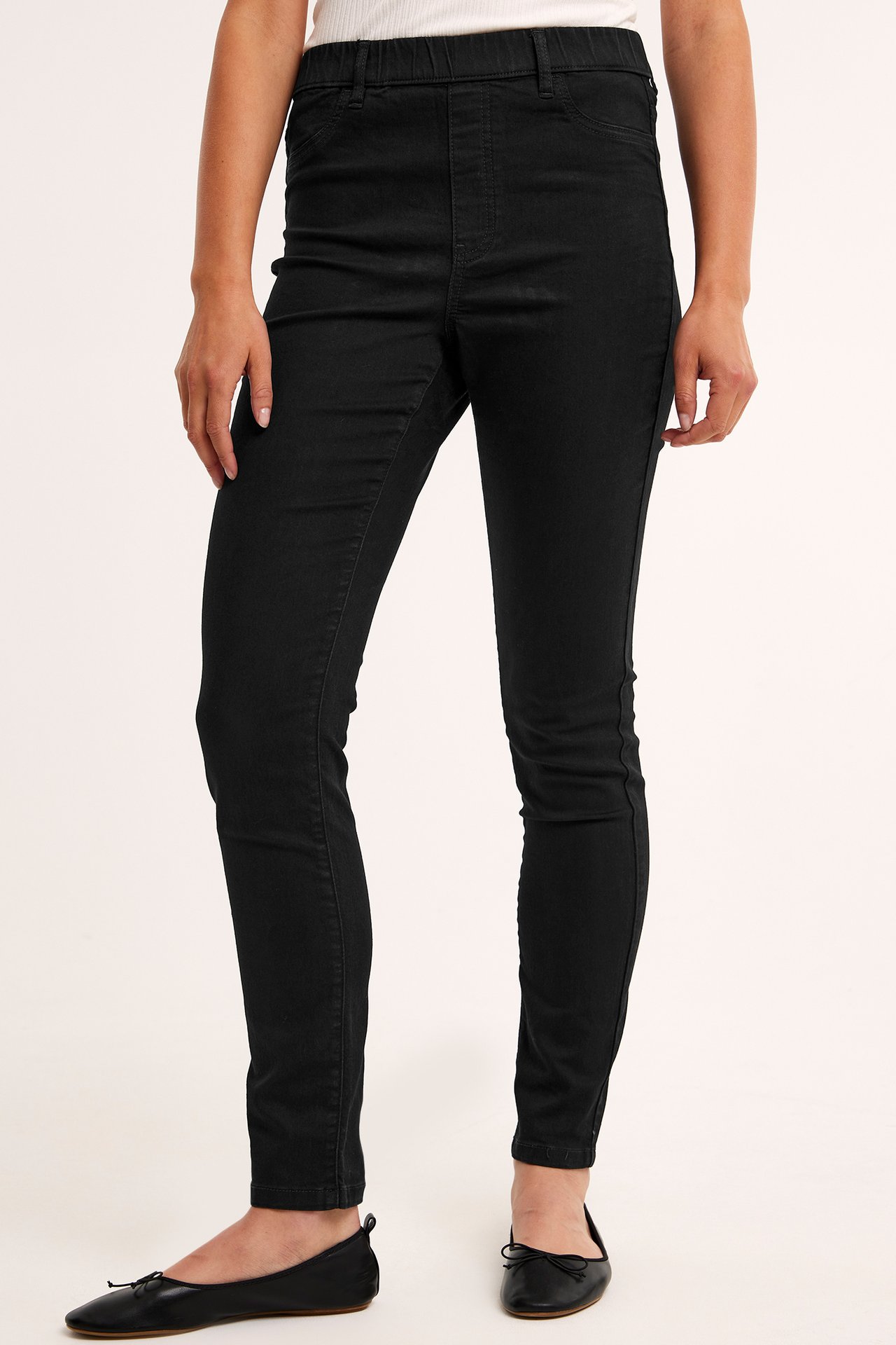 Forfra, kvinne i svarte twill-treggings med elastisk midje, hvit topp og svarte ballerinasko.