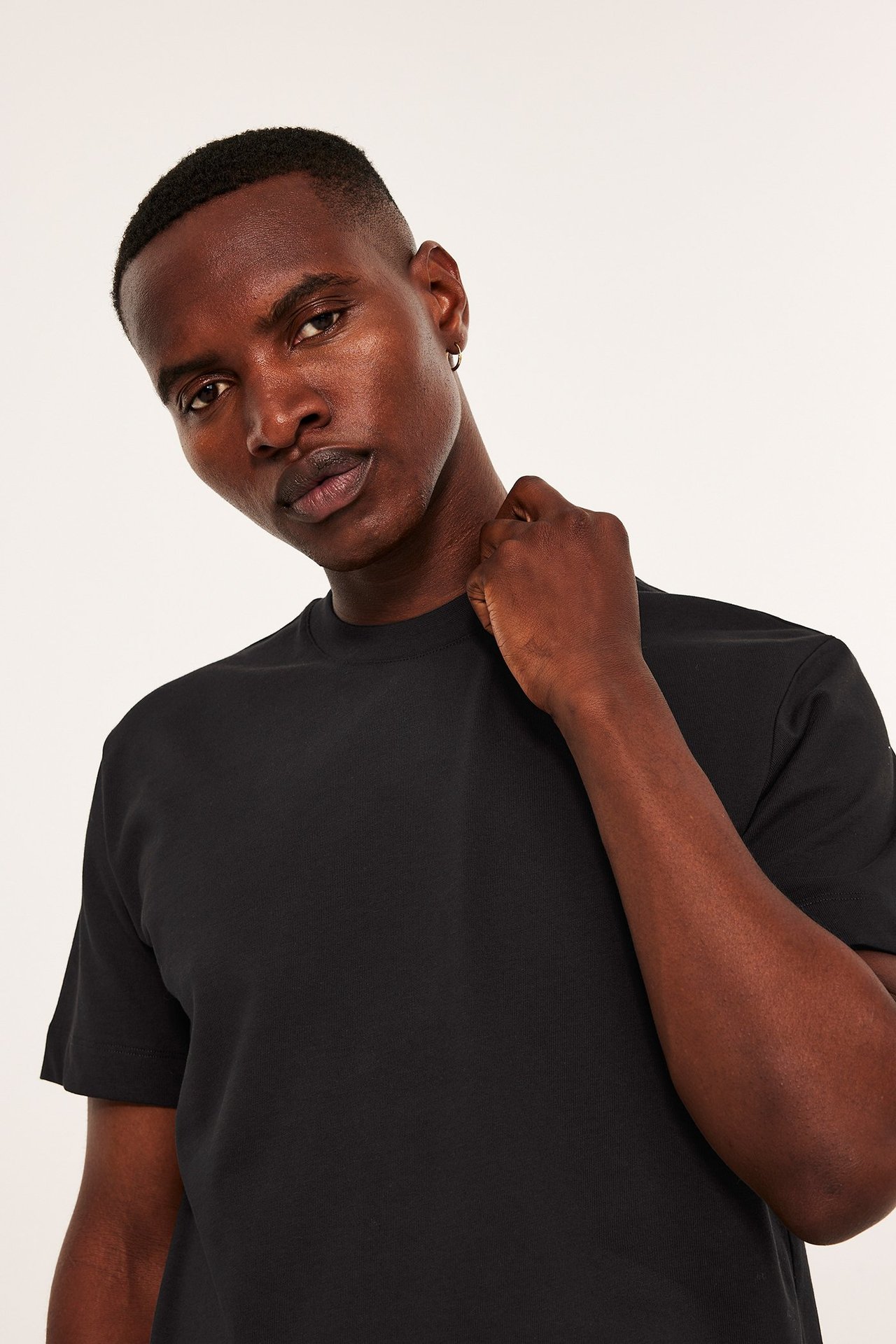 Närbild framifrån på en man i svart lös passform t-shirt med rund hals och en silverfärgad ringörhänge.