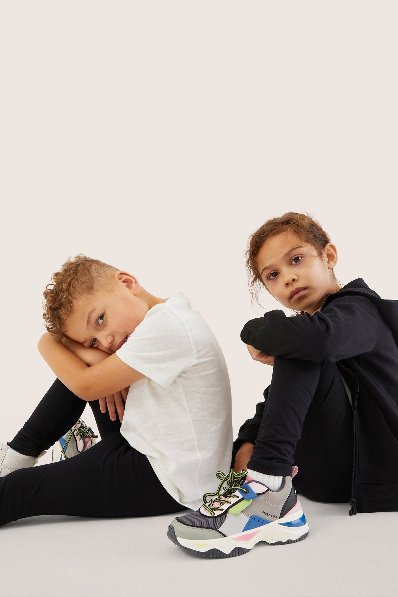 Forfra: To barn i svarte leggings, en hvit t-skjorte, en svart hettegenser og fargerike joggesko.