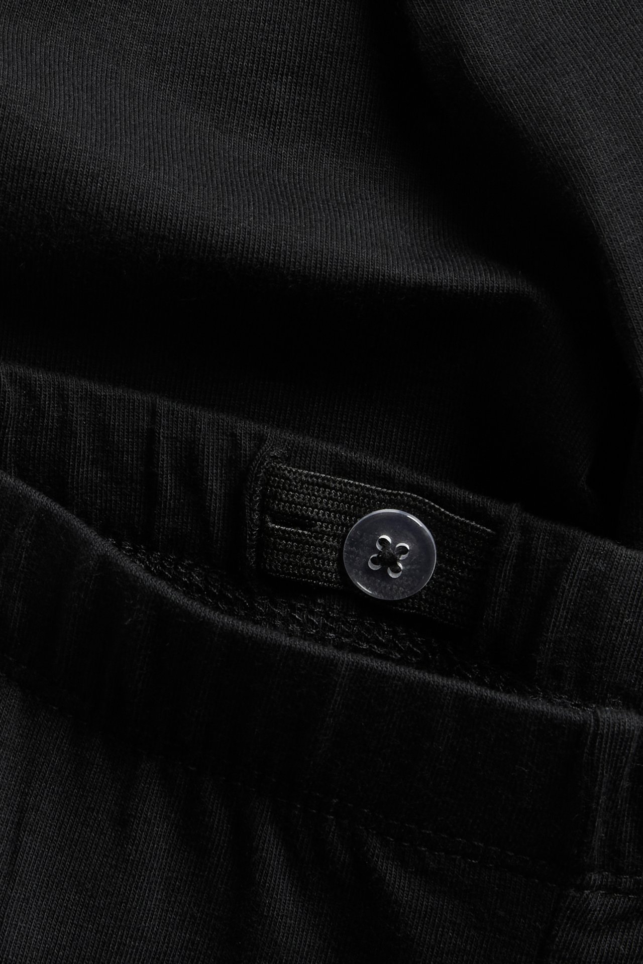 Närbild av svarta leggings för barn med justerbar resårlinning och en transparent knapp.