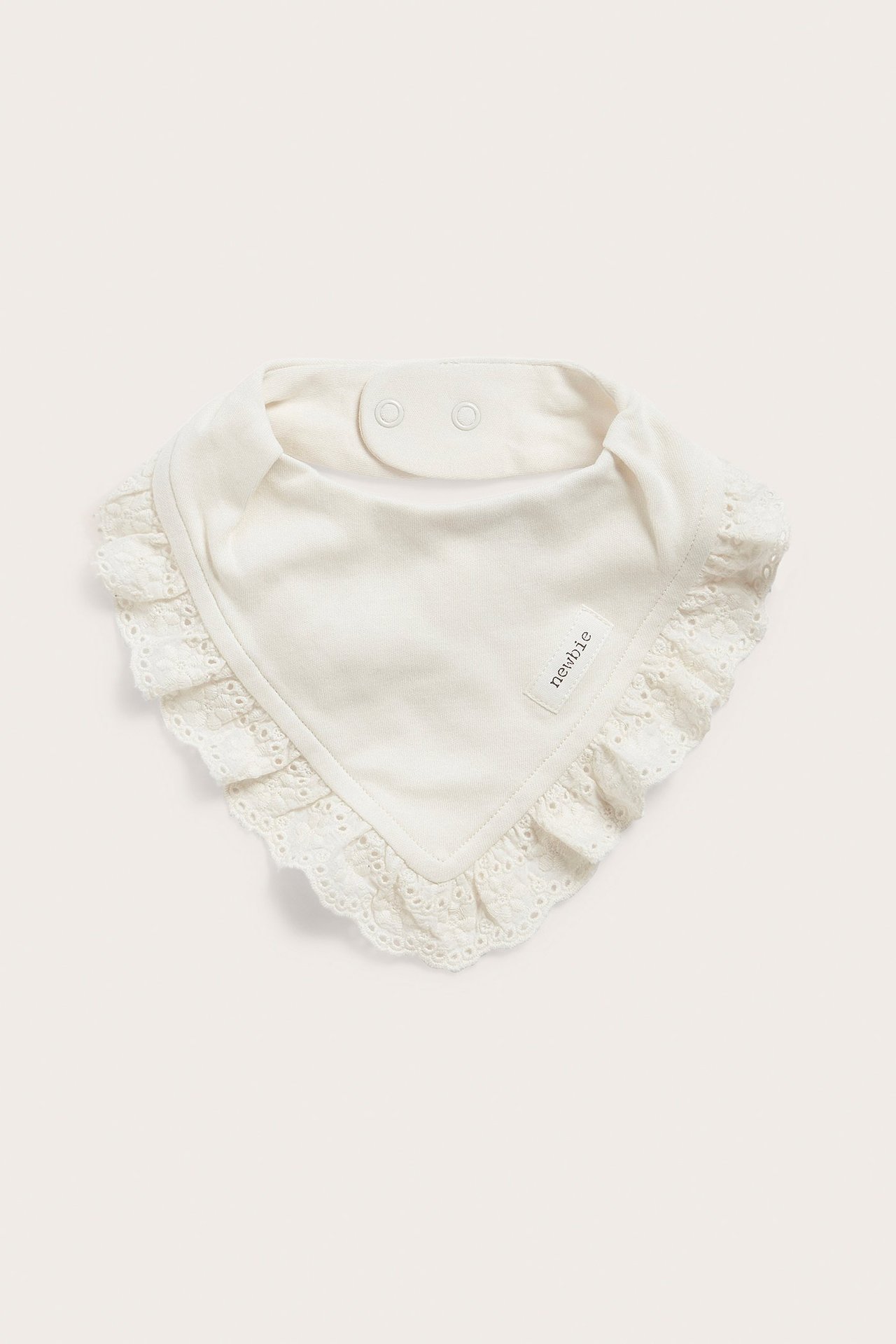Widok z przodu. Bawełniany śliniak dla niemowląt w kolorze ecru z koronkową lamówką, zapinany na dwa zatrzaski.